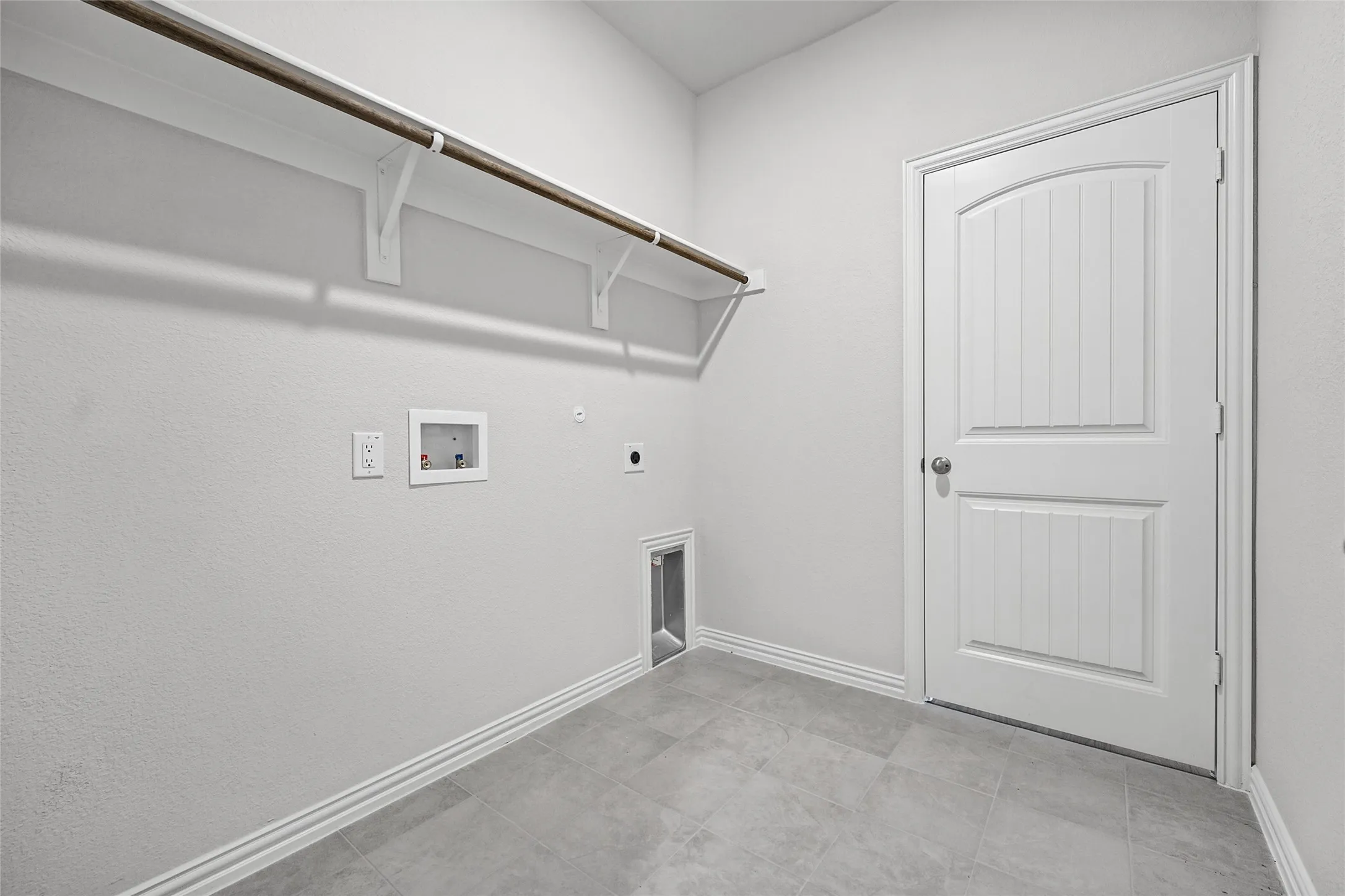 Utility room featuring tile flooring, a hanging rod with shelving, a white paneled door, and appliance hookups