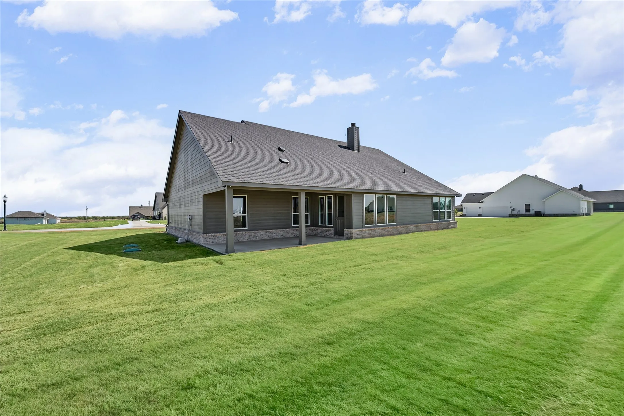 Expansive rear yard featuring a covered patio, multiple windows, and a shingle roof