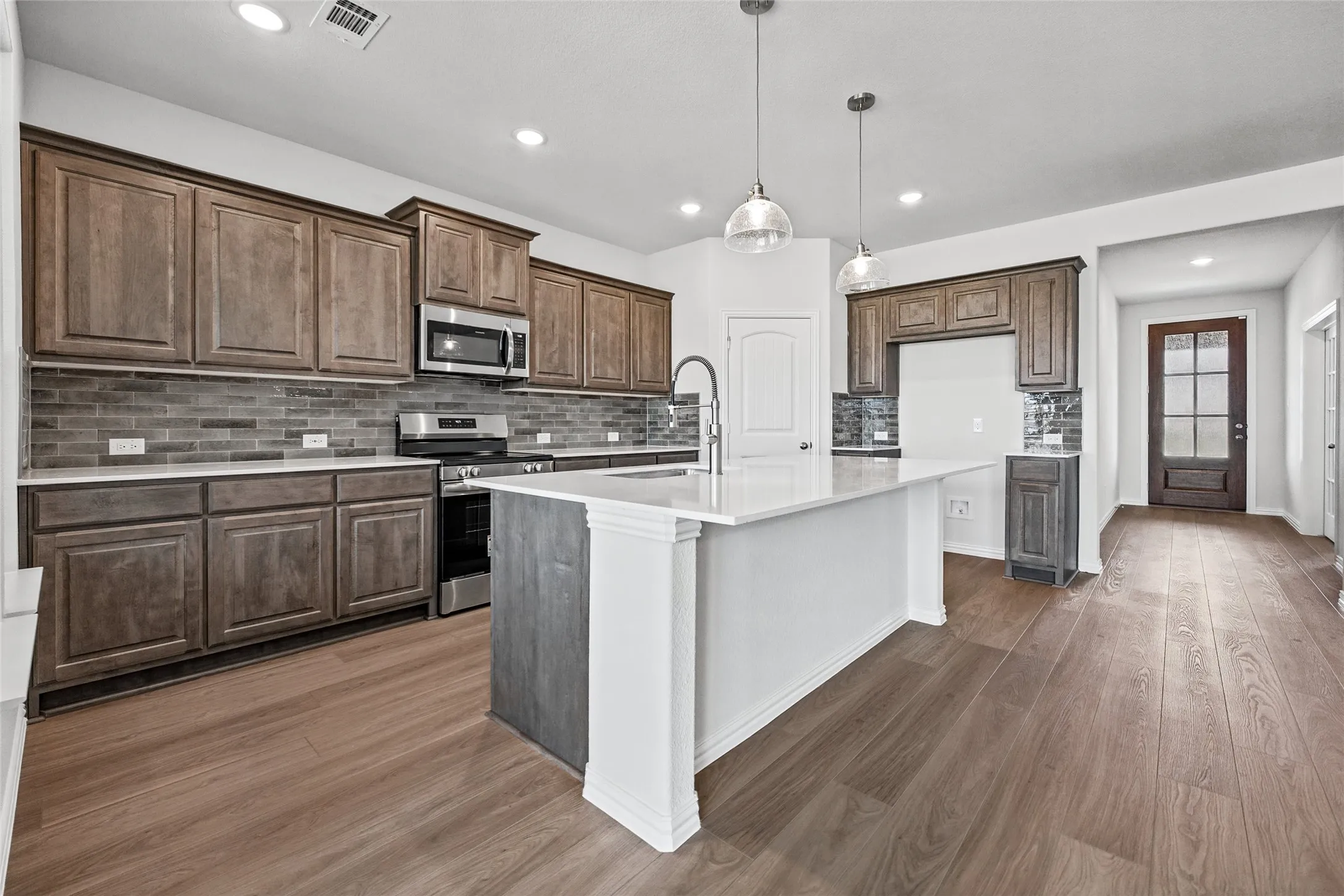 Kitchen featuring wood-finish flooring, dark wood cabinetry, a tiled backsplash, and stainless steel appliances