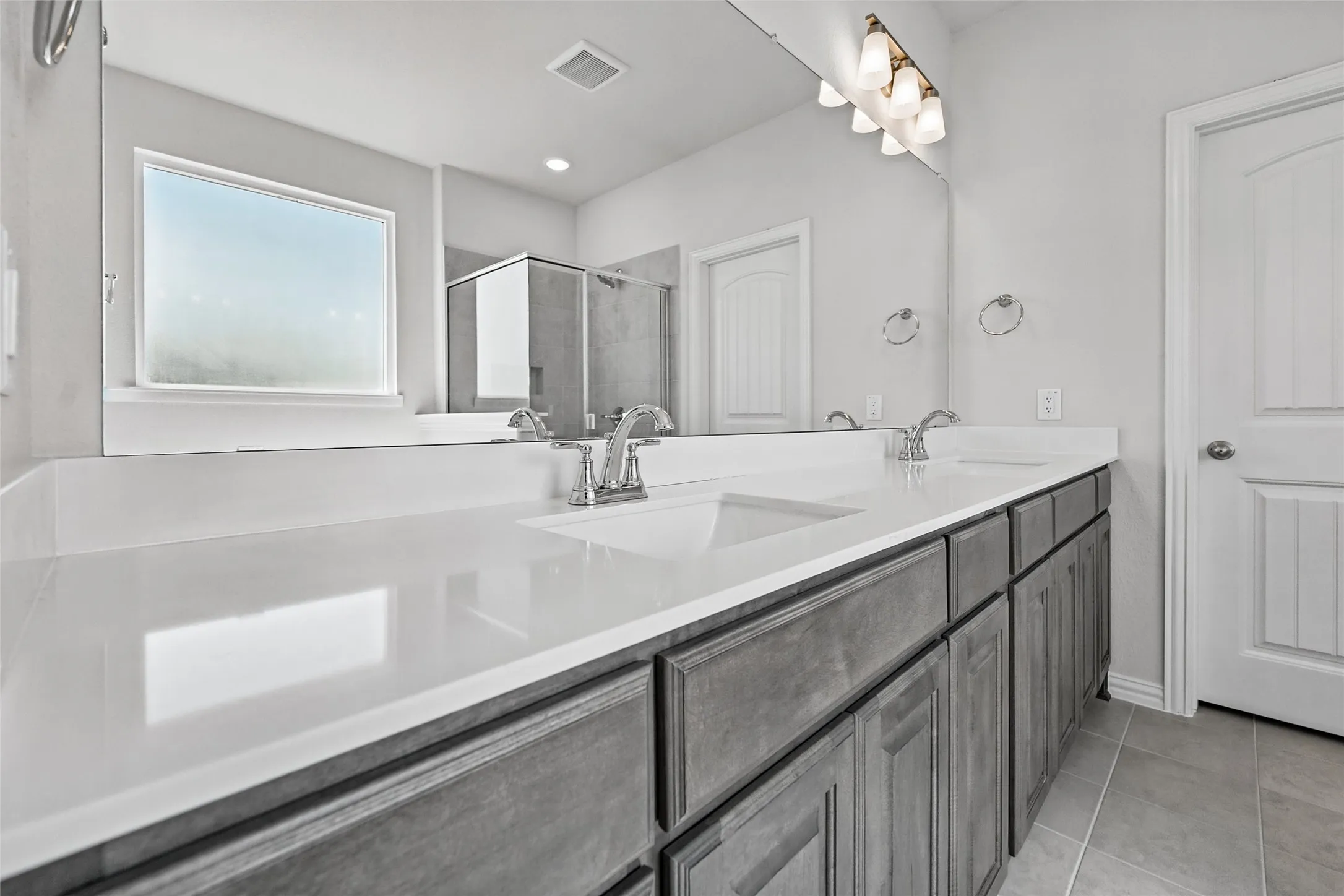 Double vanity with integrated sinks, chrome fixtures, a full-width mirror, and gray cabinetry