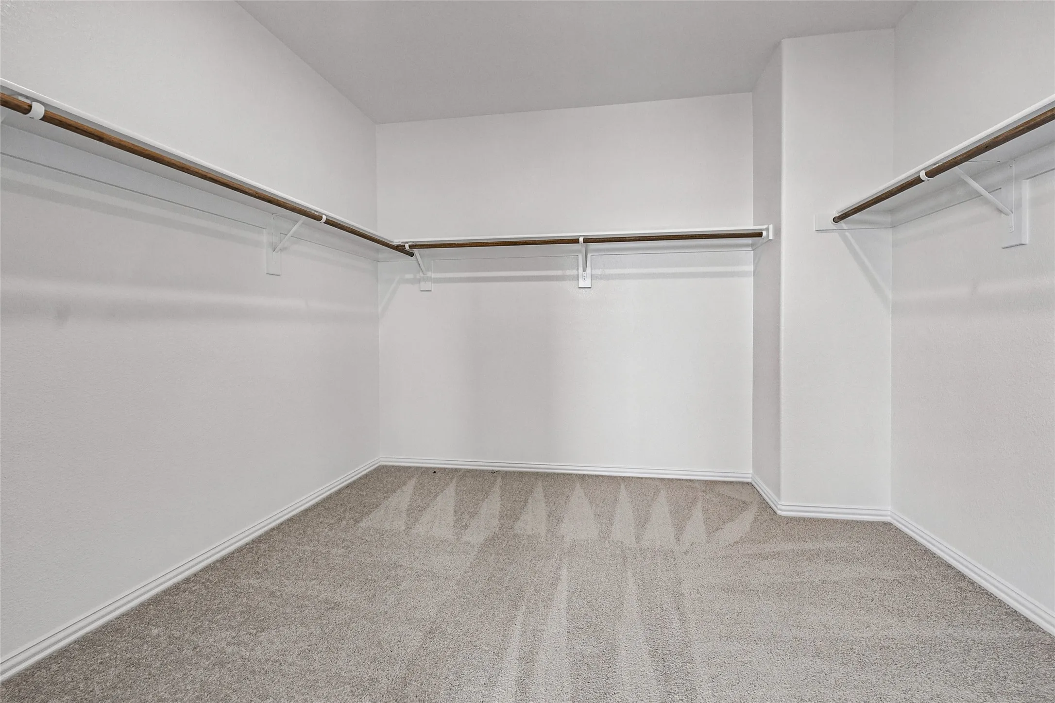 Wall-to-wall carpeting with a geometric pattern, neutral wall paint, and multiple clothing rods with shelving