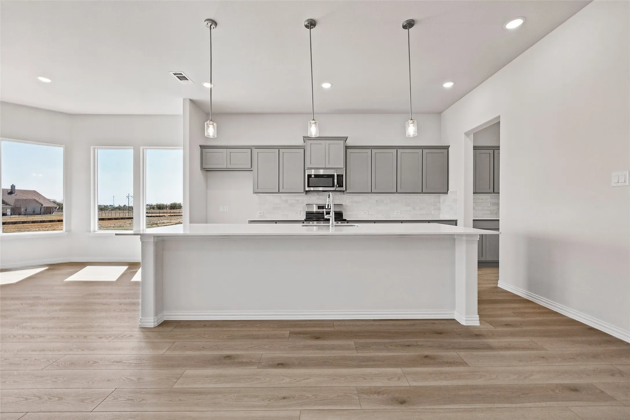 Kitchen island with a white countertop, wood-finish flooring, gray cabinetry, built-in microwave, and recessed lighting