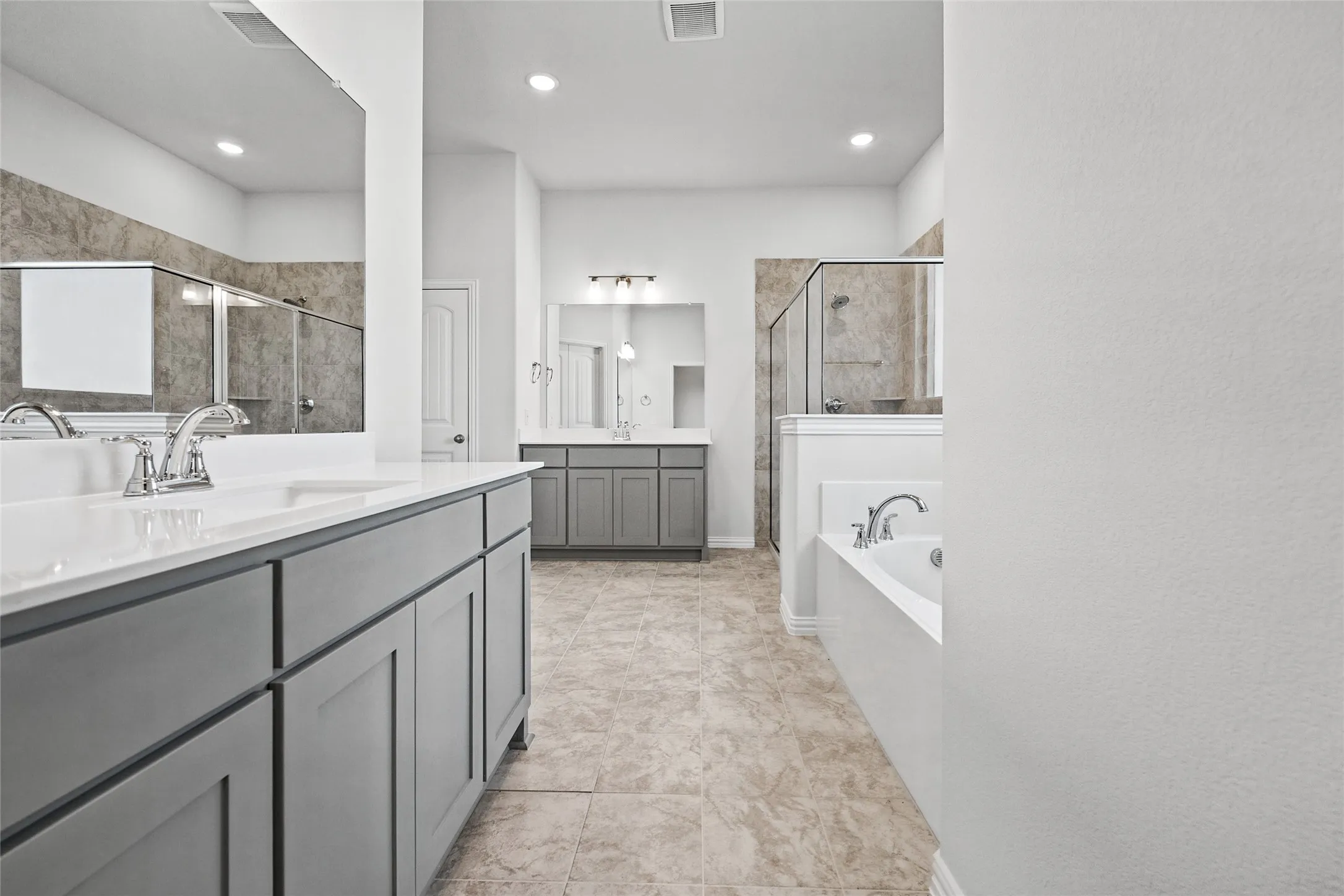 Dual vanities with white countertops, chrome fixtures, tile flooring, built-in bathtub, and a glass-enclosed shower