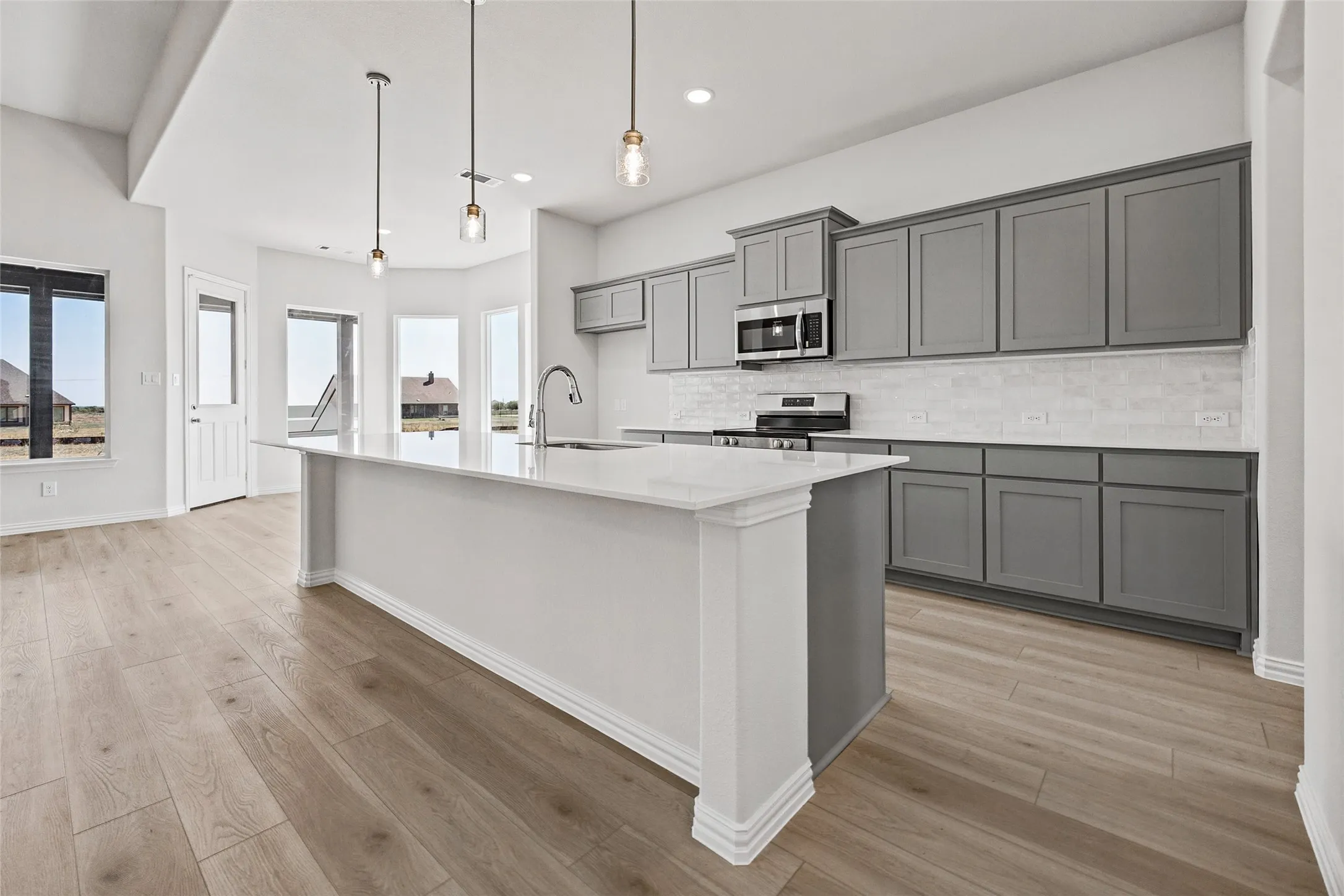 Kitchen featuring an expansive island with a white countertop, gray cabinetry, white subway tile backsplash, and wood-finish flooring