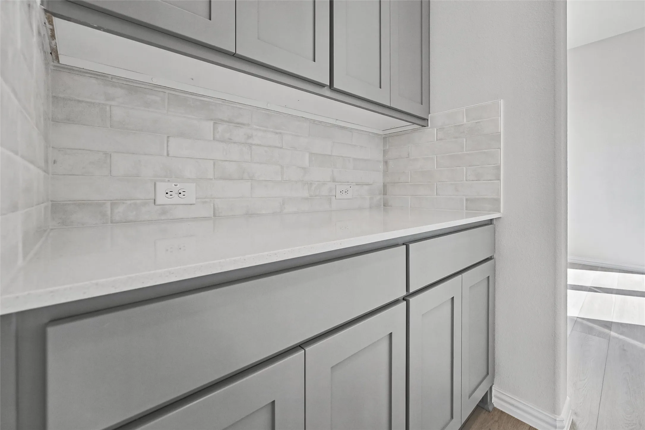 Gray shaker-style cabinetry with white countertop, subway tile backsplash, and wood-finish flooring