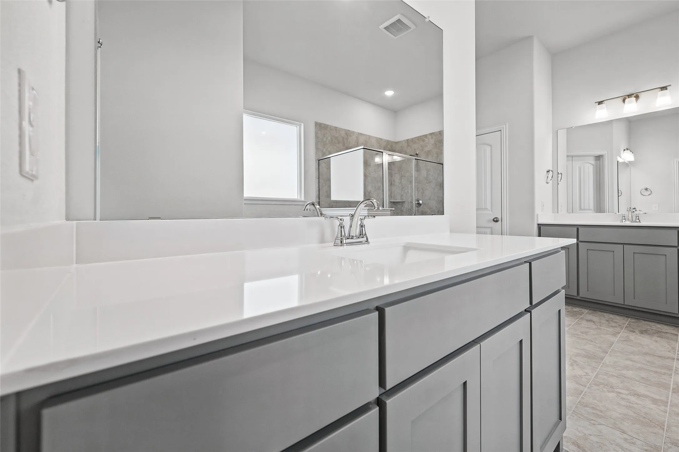 Dual vanity with integrated sinks, polished chrome fixtures, gray cabinetry, and light-toned tile flooring