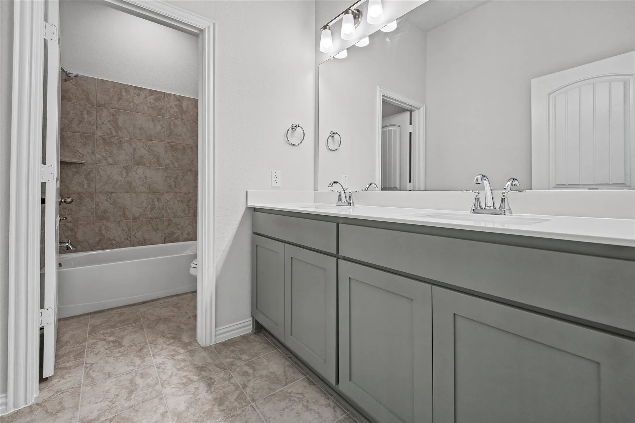 Dual vanity with undermount sinks and chrome fixtures, light-toned countertop, gray shaker-style cabinetry, and tile flooring