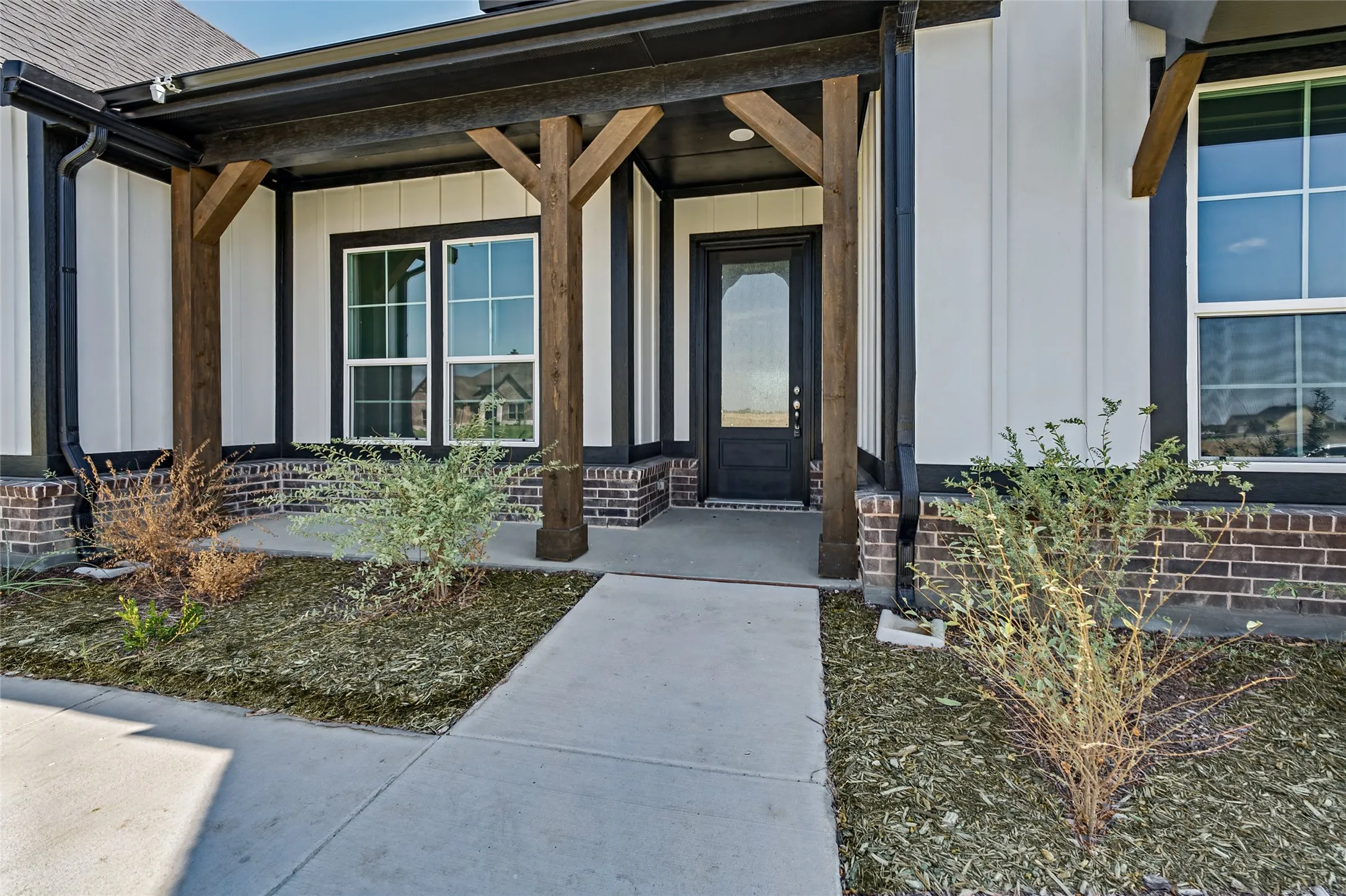 Covered entry with dark wood posts, a solid panel door with a decorative glass insert, and brick skirting