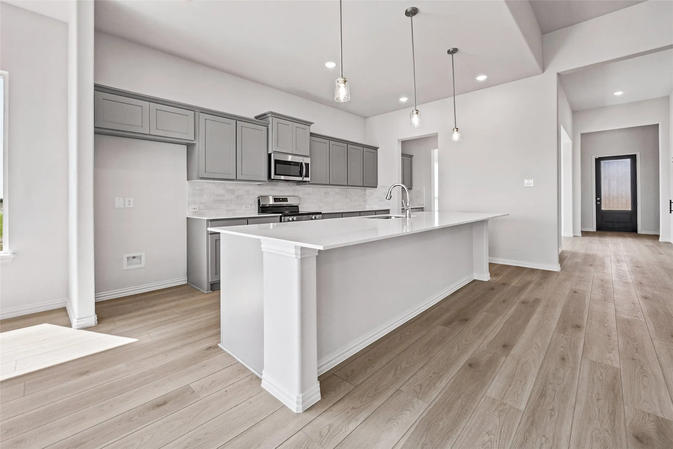 Kitchen featuring an expansive island with a stainless steel faucet, grey cabinetry, stainless steel appliances, and wood-finish flooring