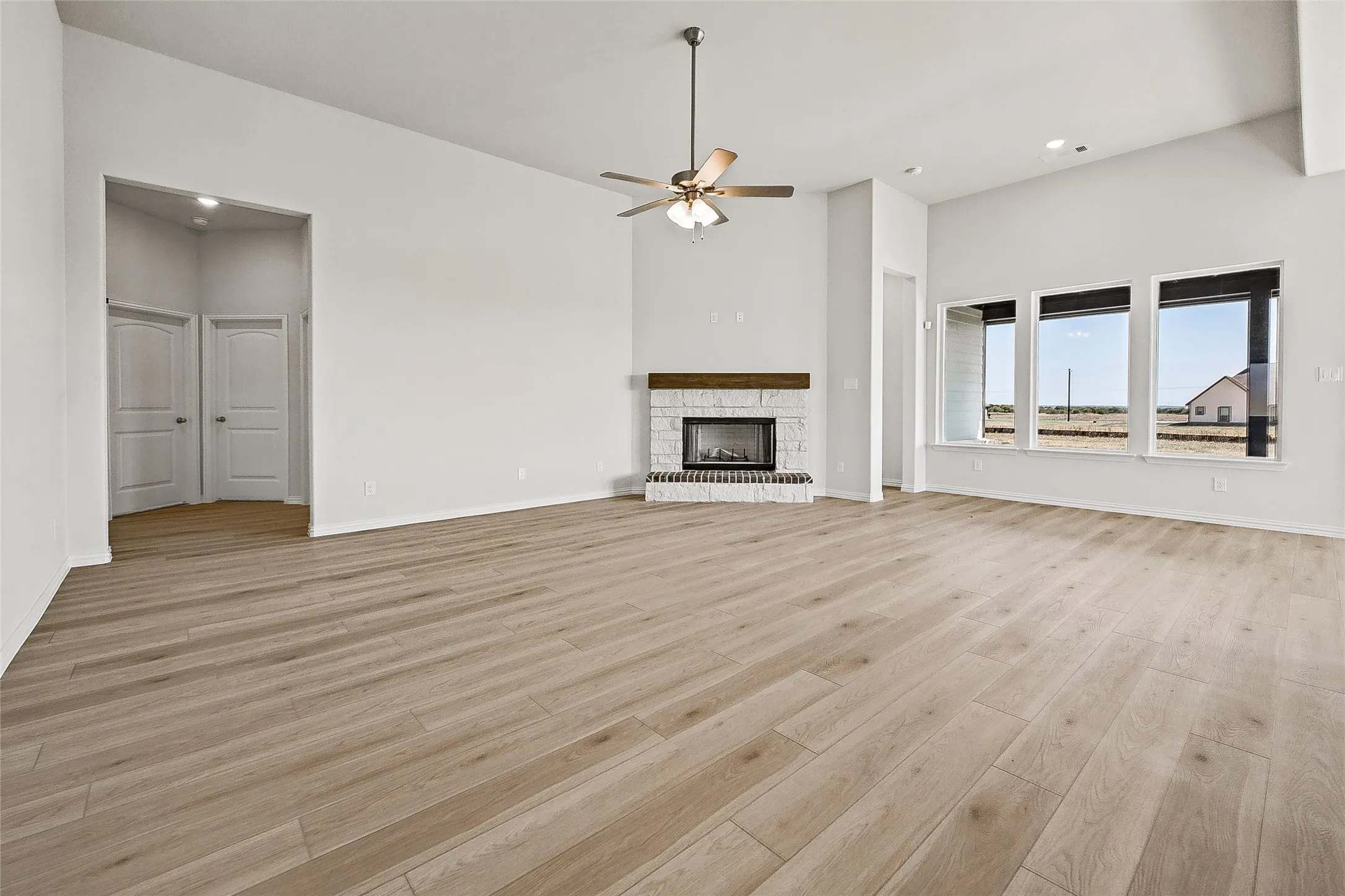 Vaulted ceilings with a ceiling fan, wood-finish flooring, a stone-surround fireplace with a wood mantle, and a wall of windows
