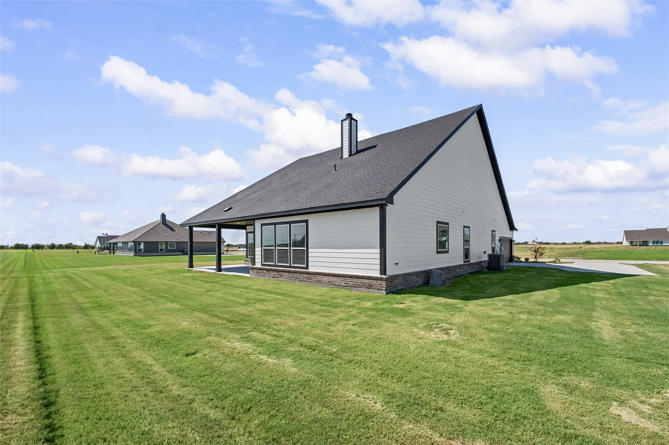 Exterior featuring a pitched roof, dark shingles, white siding, and a covered patio