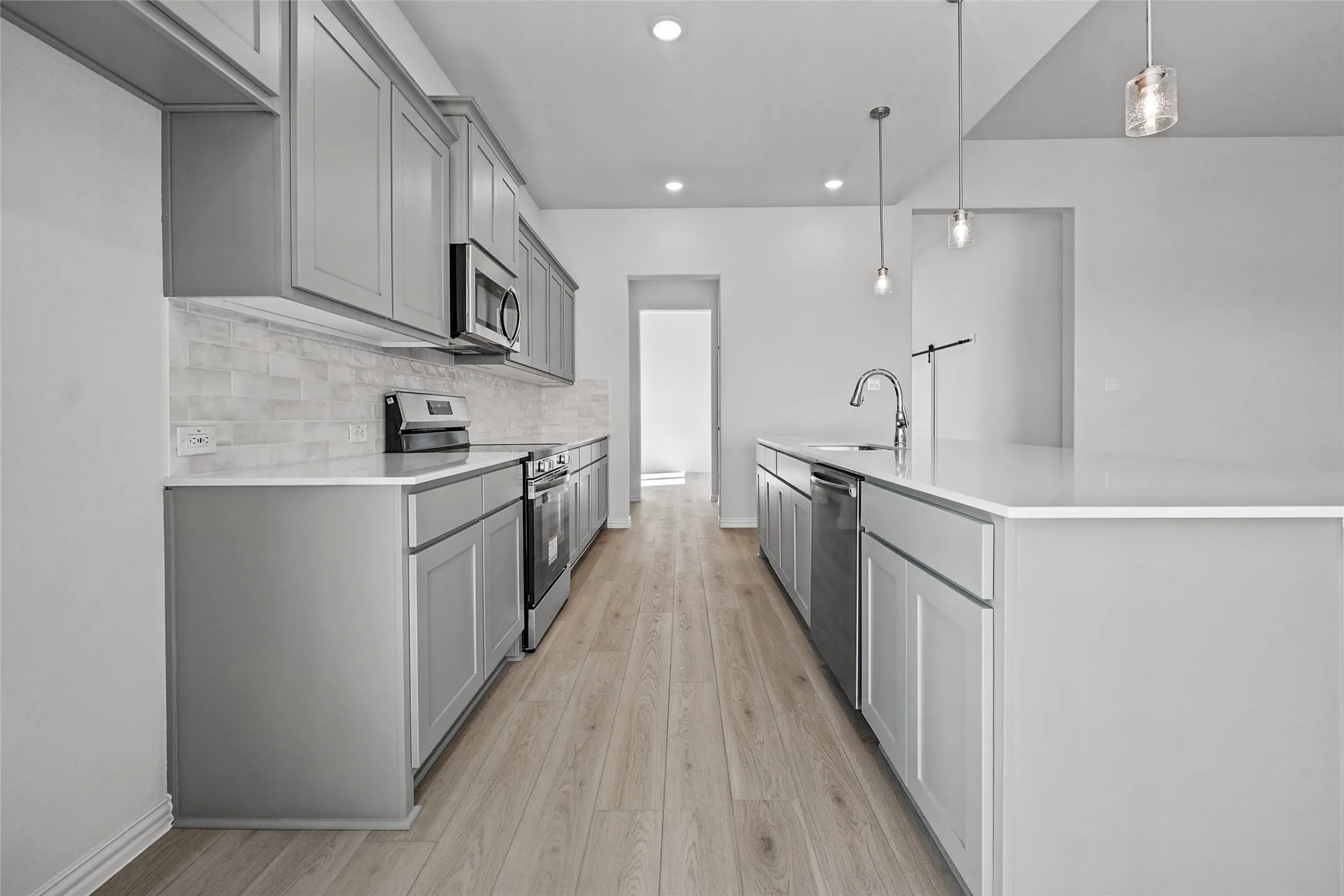 Kitchen featuring gray shaker-style cabinetry, stainless steel appliances, a white subway tile backsplash, and light wood-finish flooring