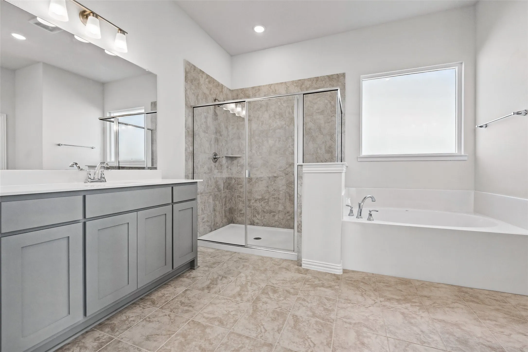 Grey vanity with white countertop, large mirror, walk-in shower with tiled walls, separate soaking tub, and tile flooring