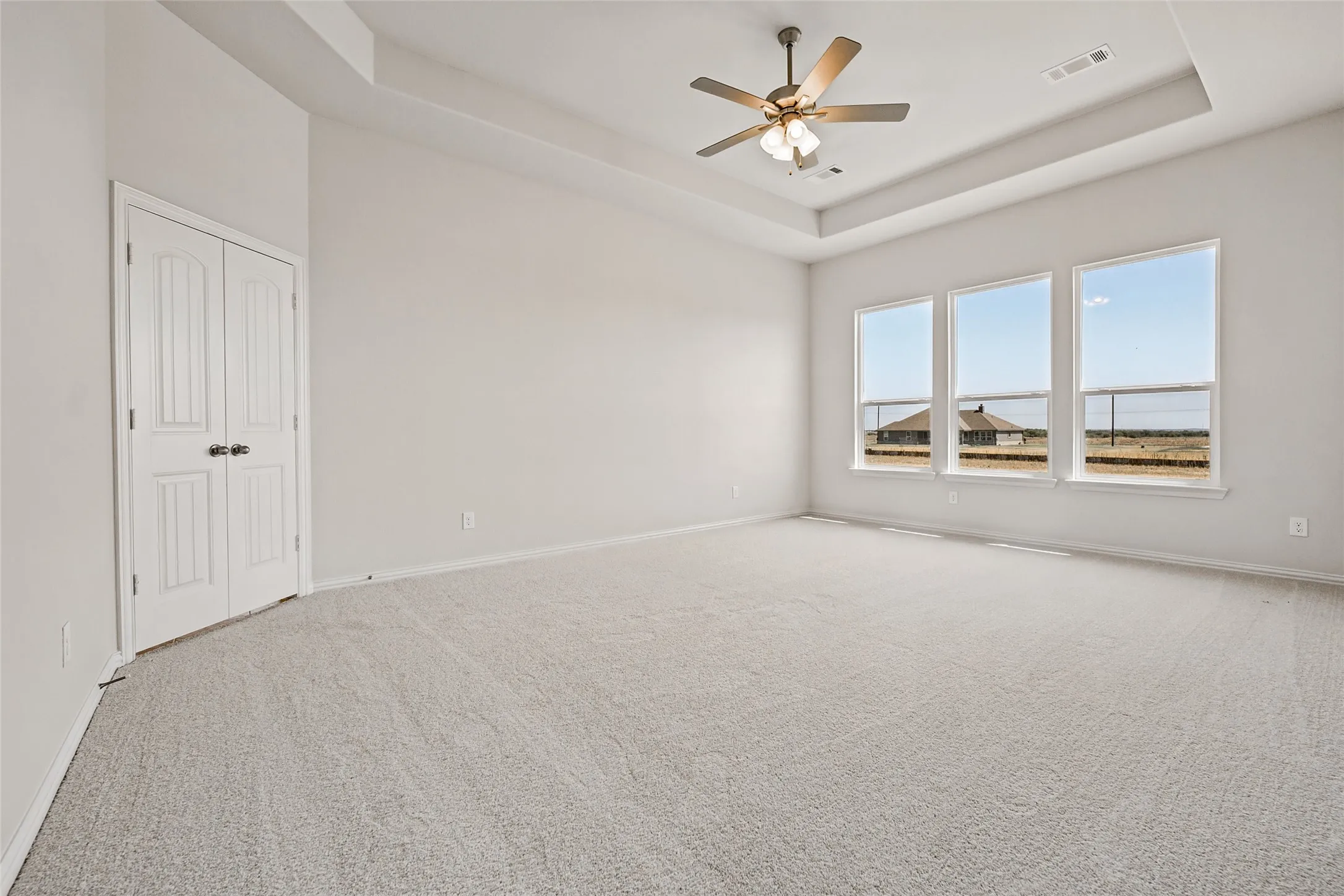 Spacious room featuring light-toned carpet flooring, a tray ceiling, and a ceiling fan