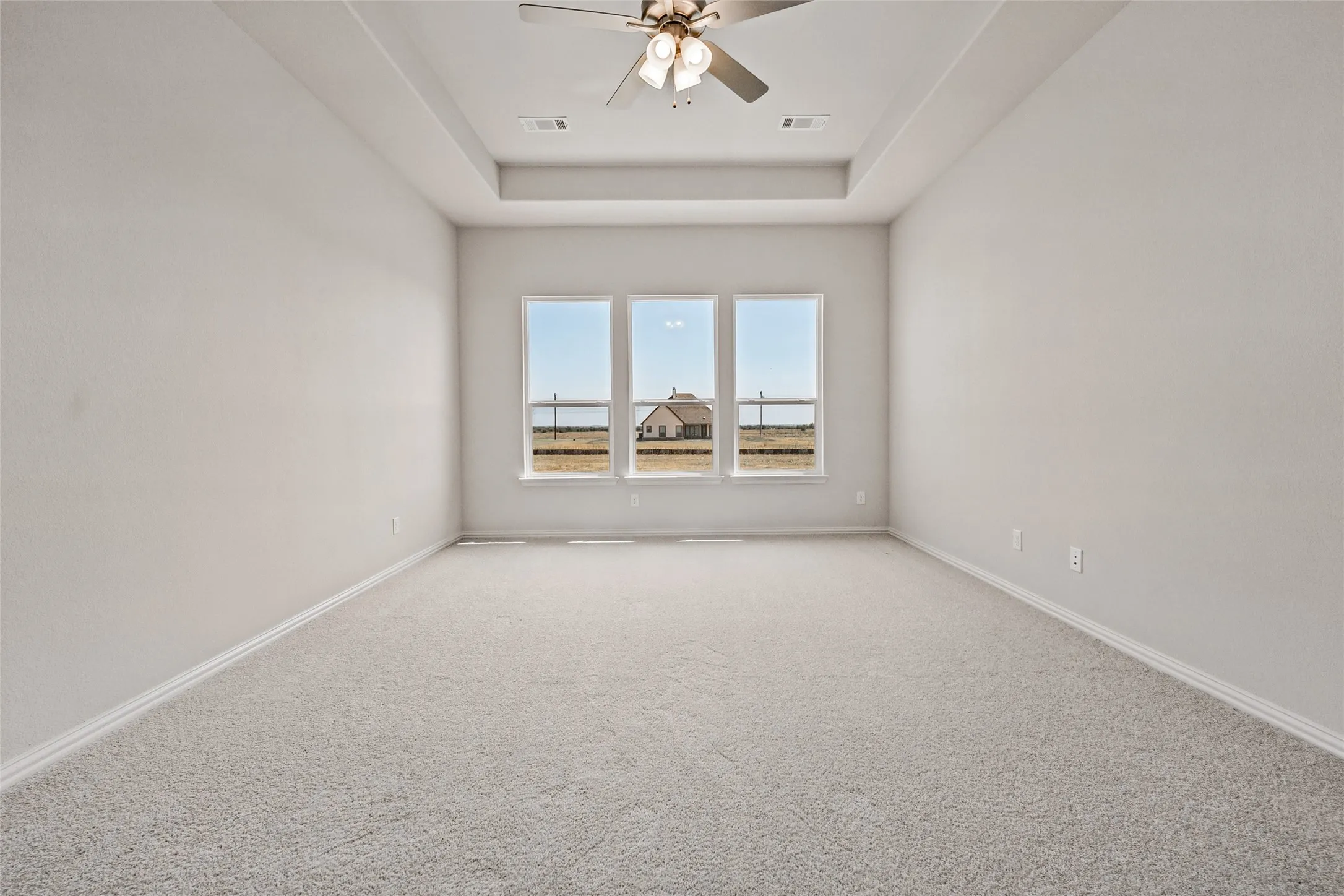 Recessed ceiling with an integrated ceiling fan, three pane windows, and light gray carpet flooring
