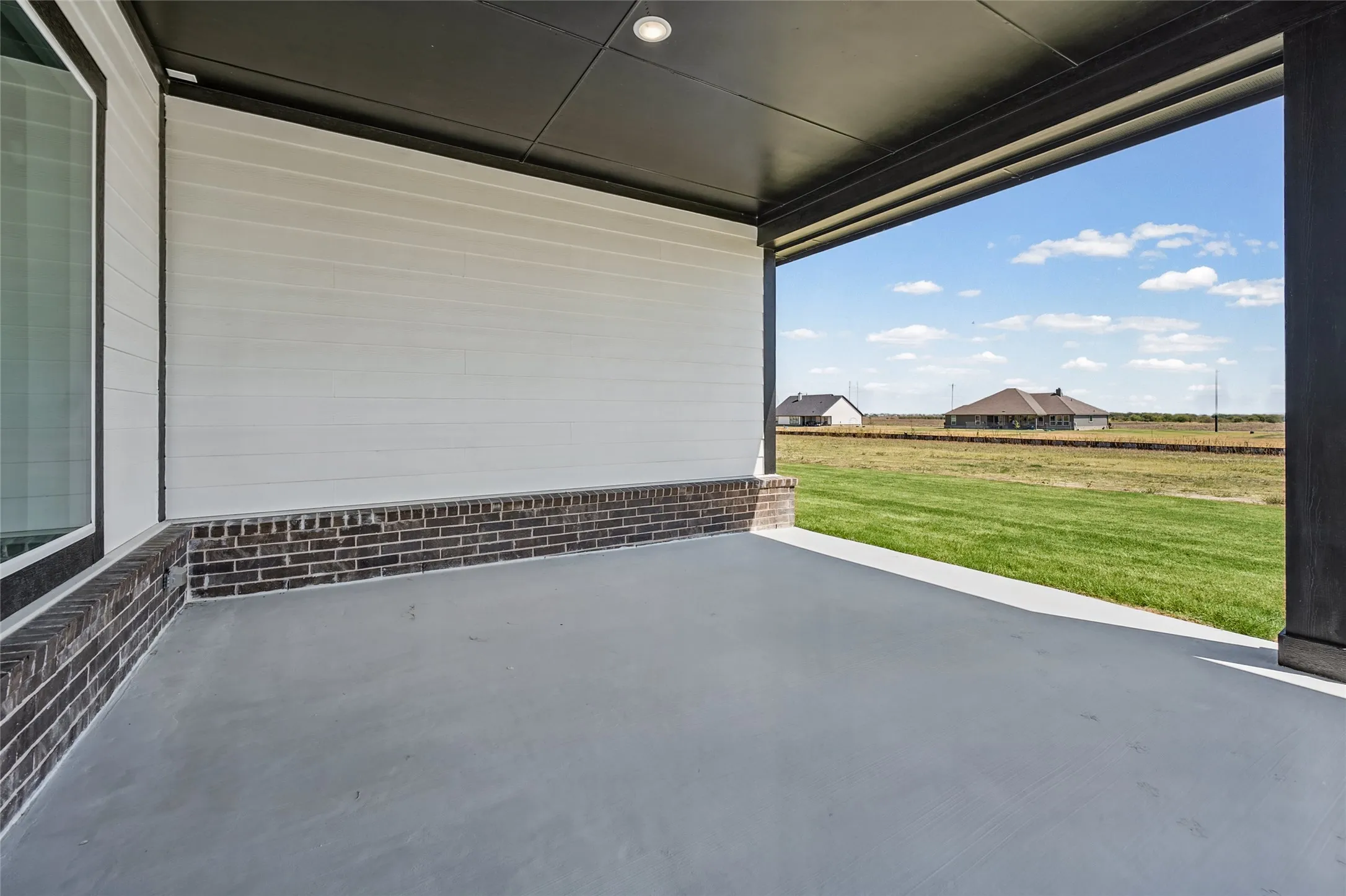 Covered patio featuring a concrete surface, white siding, and dark brick detailing