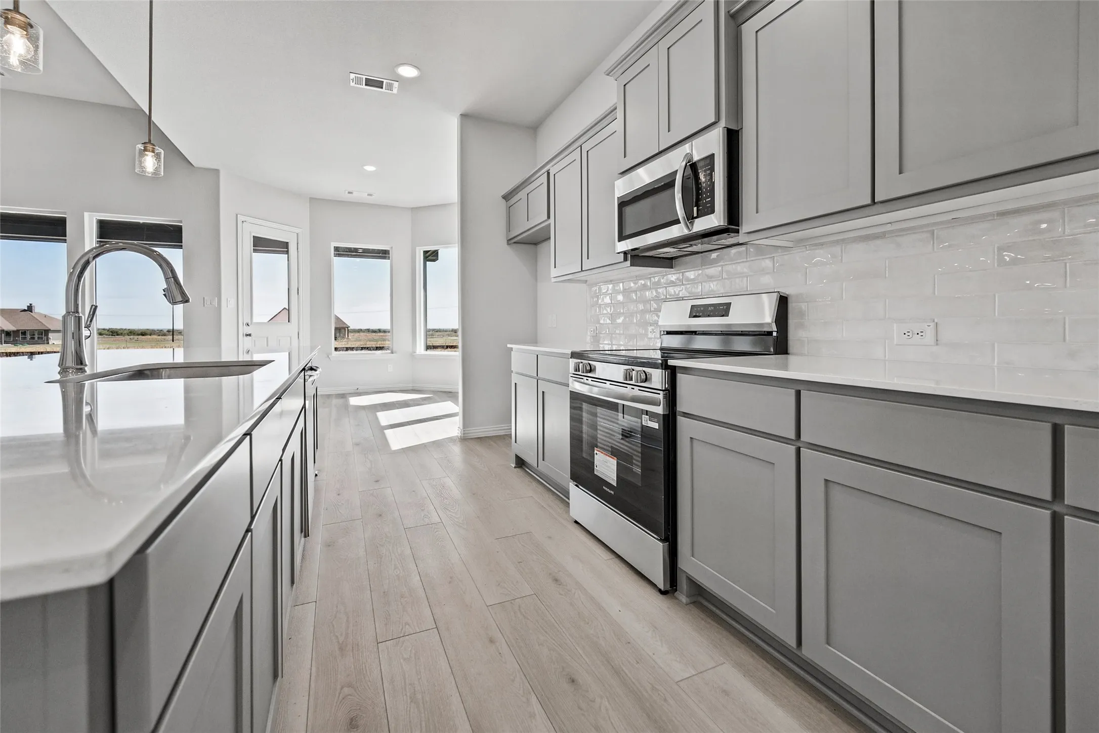 Kitchen featuring wood-finish flooring, light gray cabinetry, stainless steel appliances, and a white subway tile backsplash