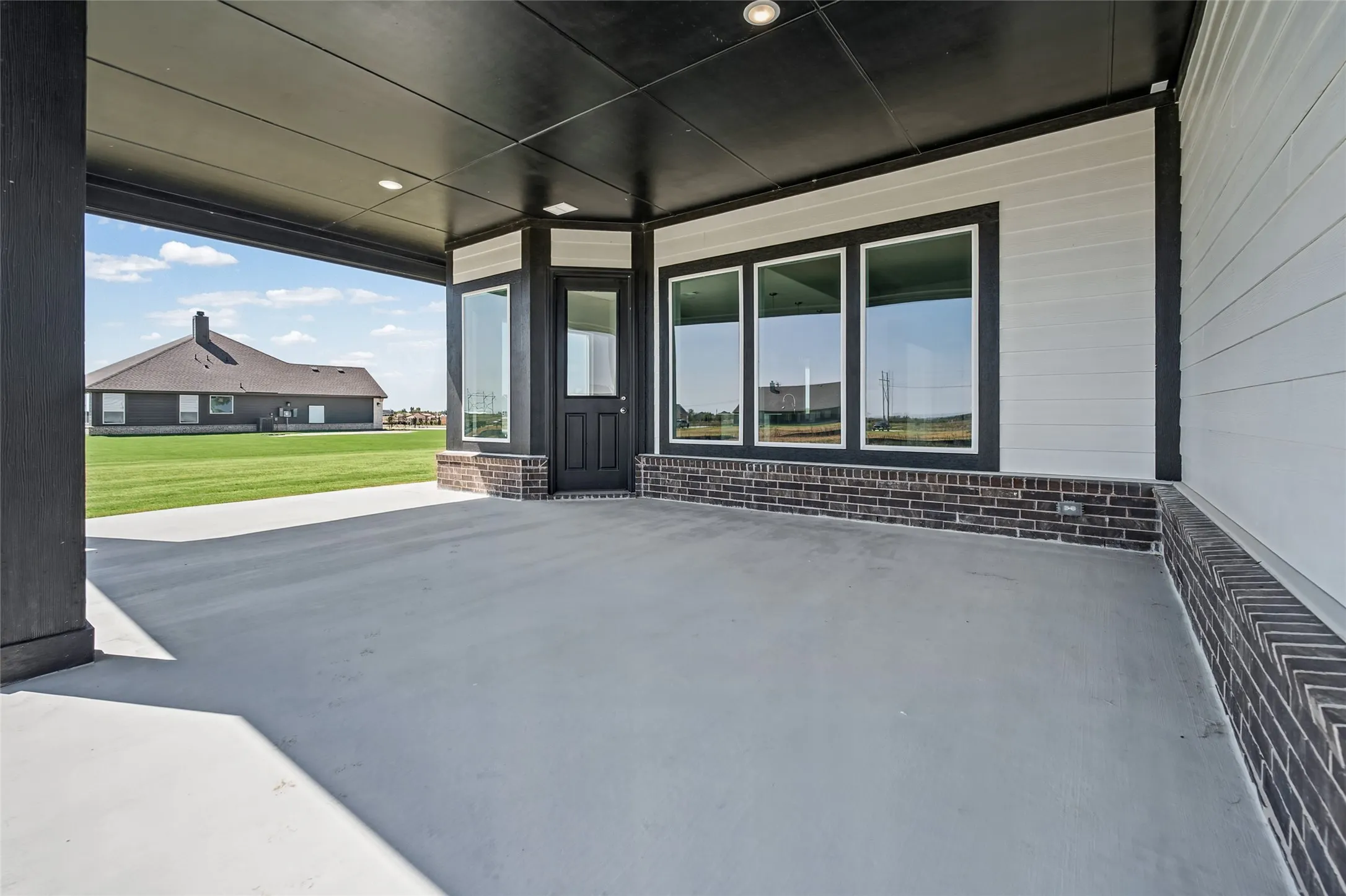 Spacious covered patio with a concrete surface, recessed lighting, and a brick base