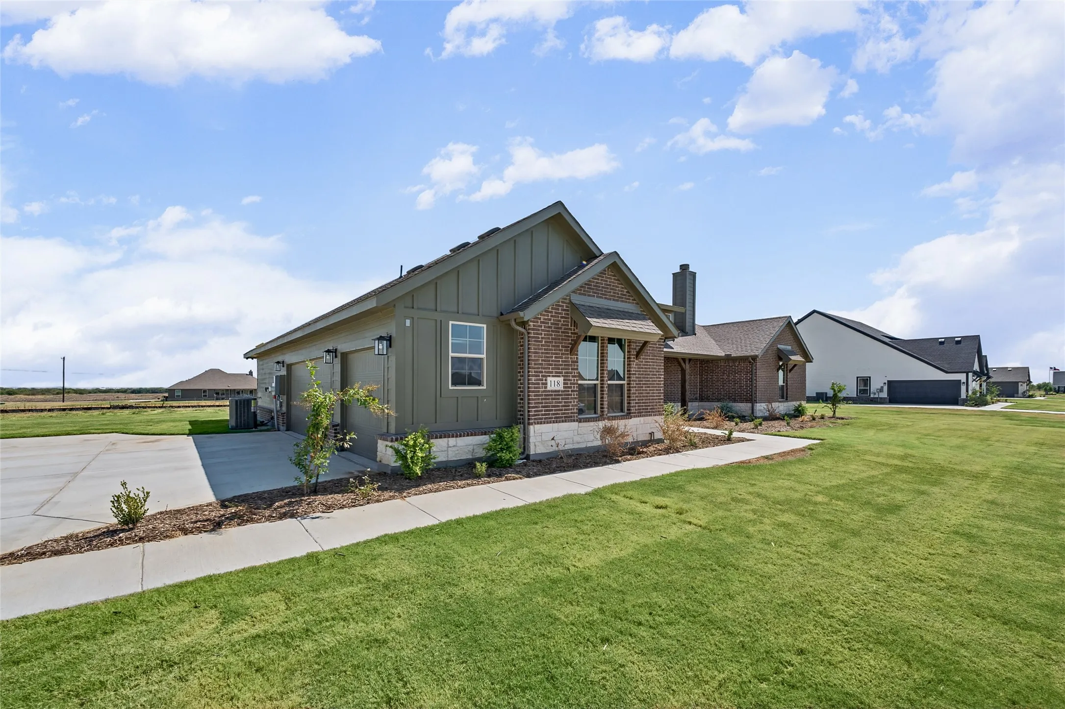 Brick and board-and-batten exterior with an attached two-car garage, concrete driveway, and front sidewalk