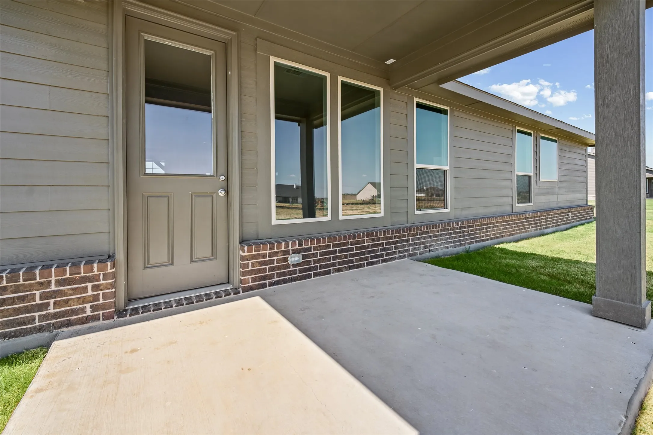 Concrete patio with a covered area, surrounded by a brick and siding exterior, featuring multiple windows and a glass-paneled door