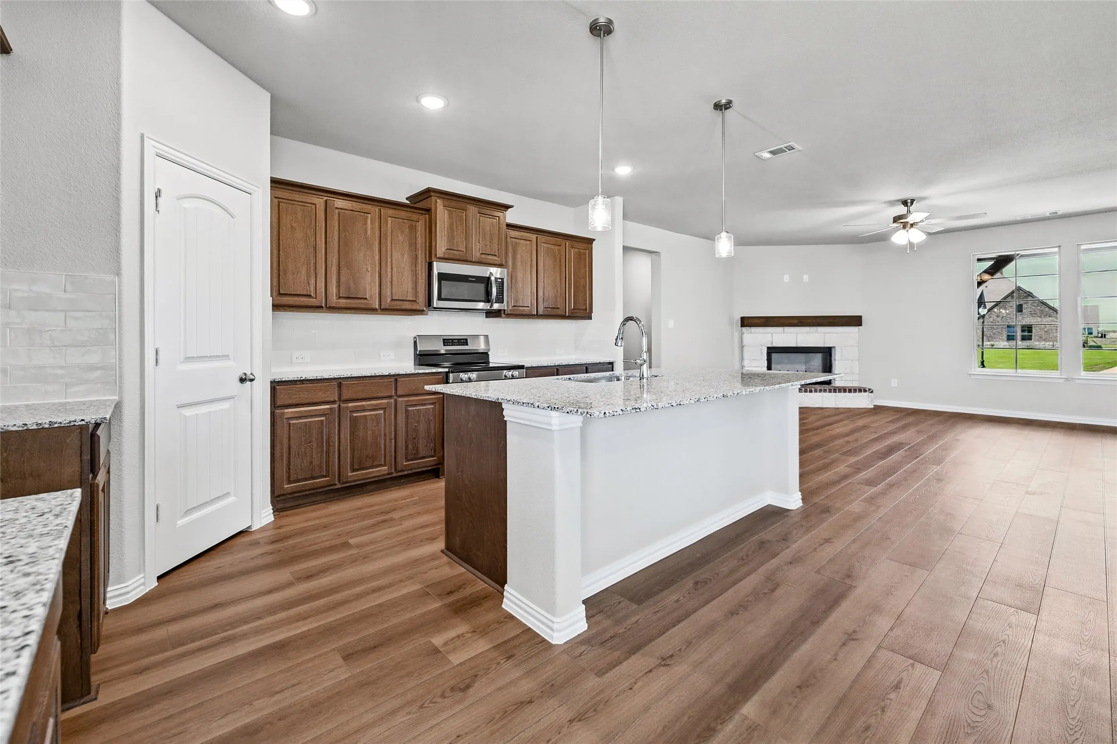 Kitchen featuring wood-finish flooring, granite countertops, an island with pendant lighting, and stainless steel appliances