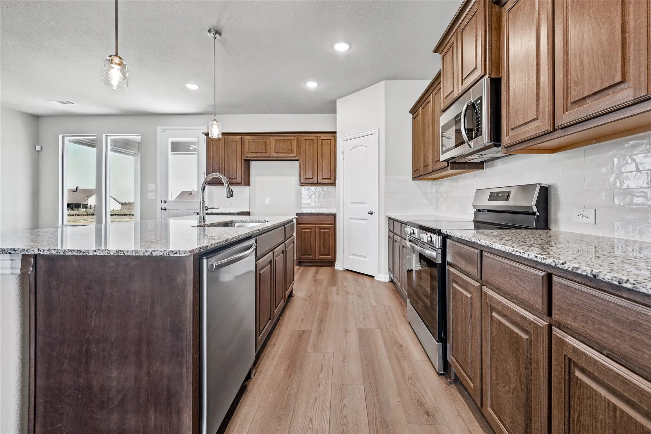 Spacious kitchen featuring an expansive island, stainless steel appliances, wood-finish flooring, recessed lighting, and a subway tile backsplash