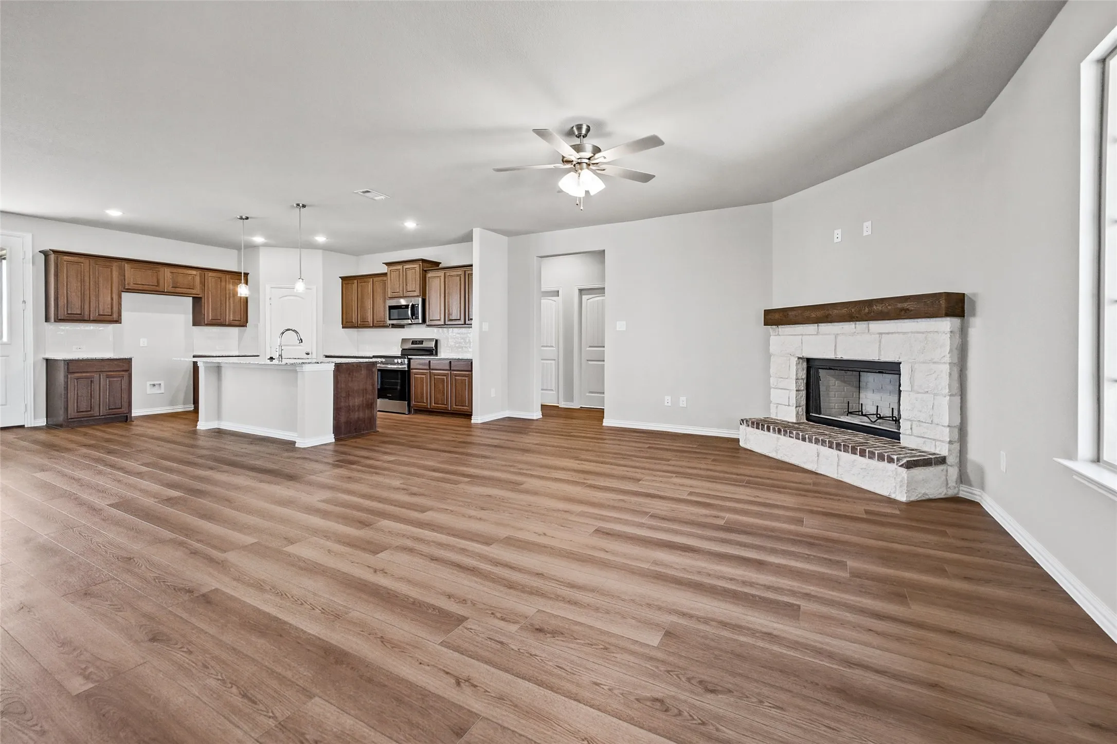 Open-concept living area with wood-finish flooring, a stone fireplace with a wood mantle, and a ceiling fan
