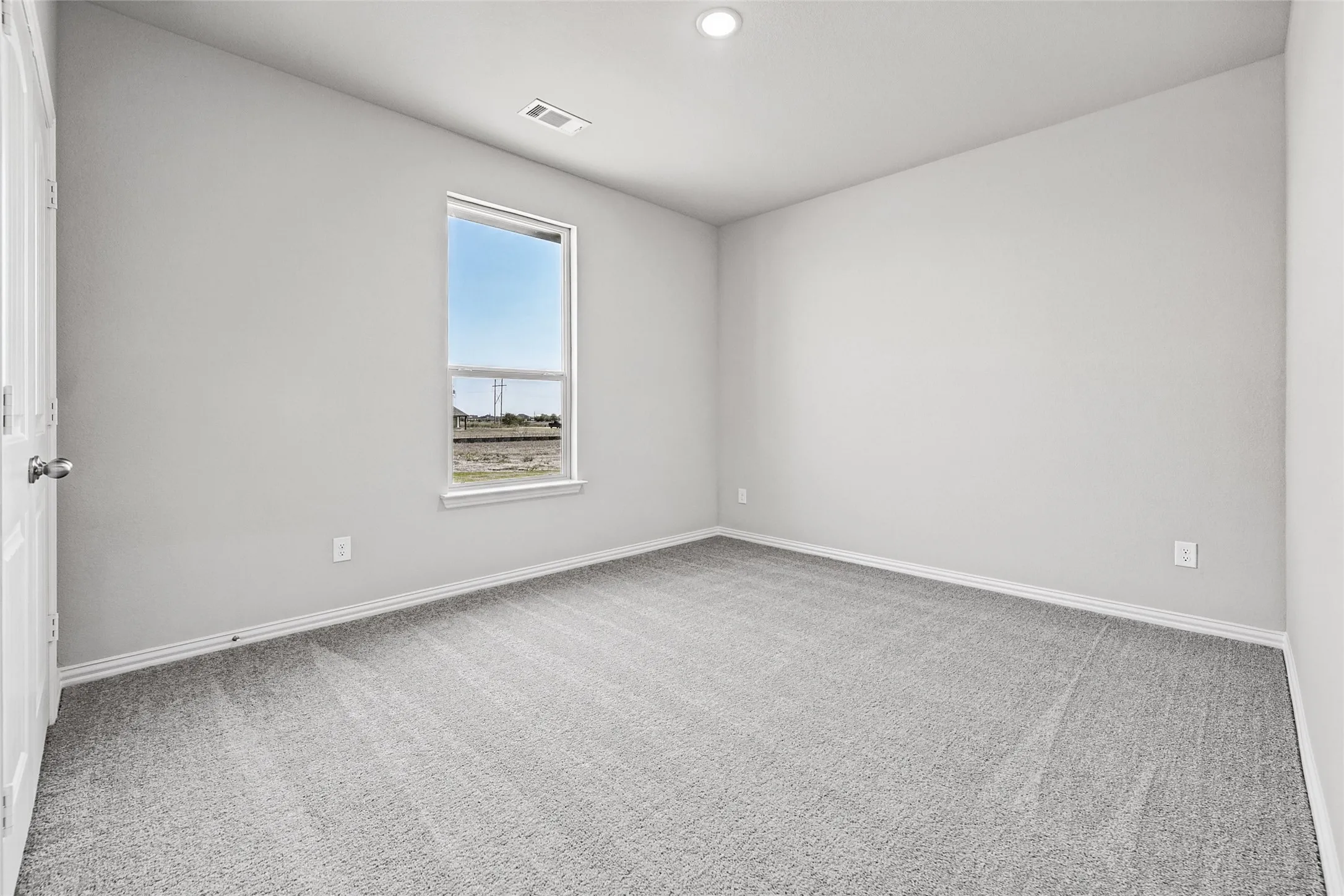 Recessed ceiling lighting, light gray wall paint, gray carpeting, and a white framed window