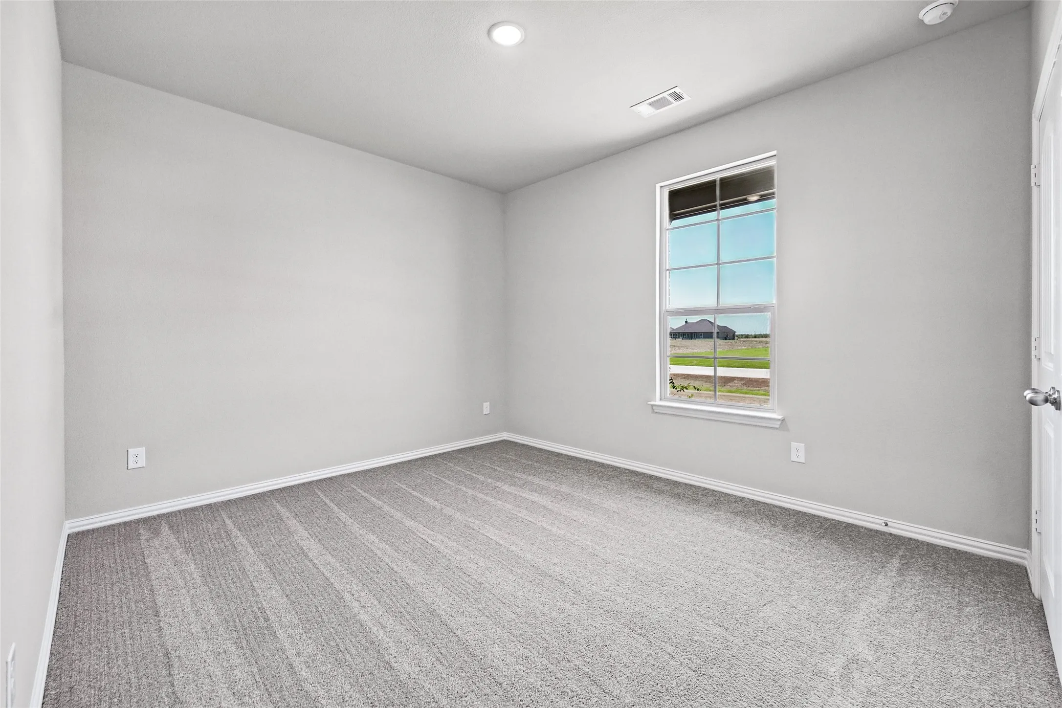 Neutral gray wall paint, gray patterned carpet, white window trim, white painted door, and recessed lighting