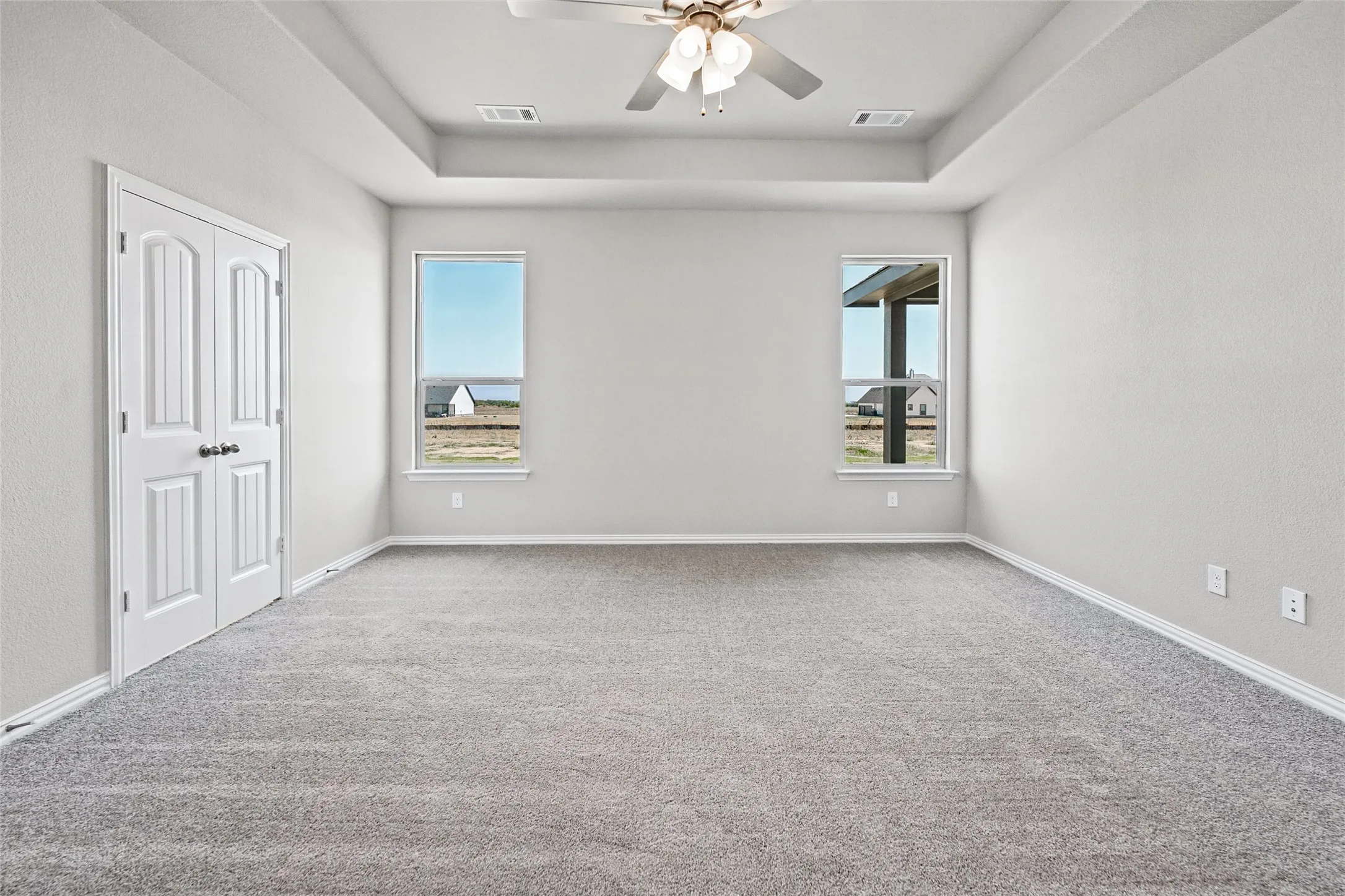 Recessed ceiling with an attached ceiling fan, dual windows, and light grey carpeting