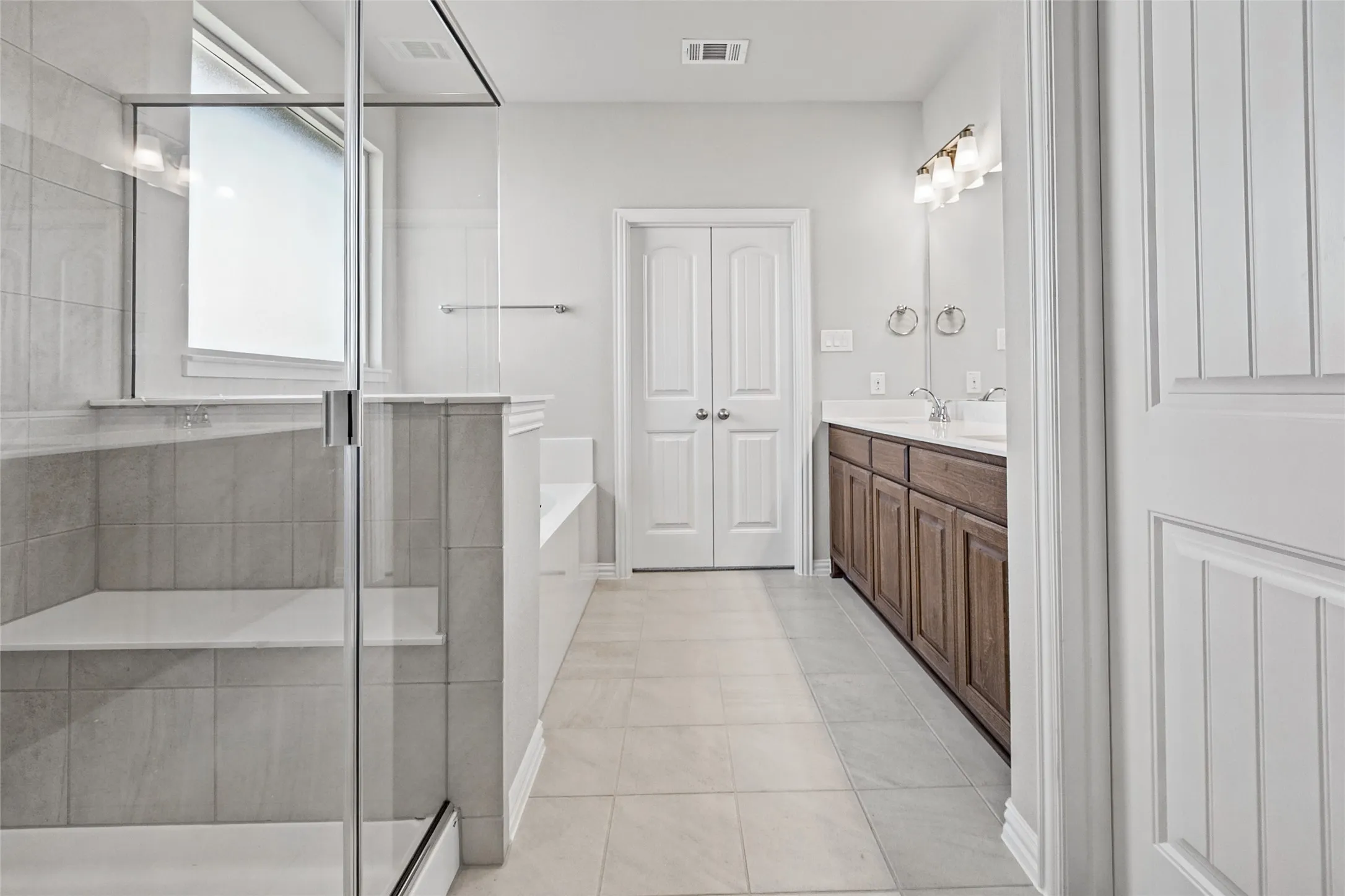 Glass-enclosed shower with a built-in bench, freestanding bathtub, dual vanity with undermount sinks, and wood-finish cabinetry