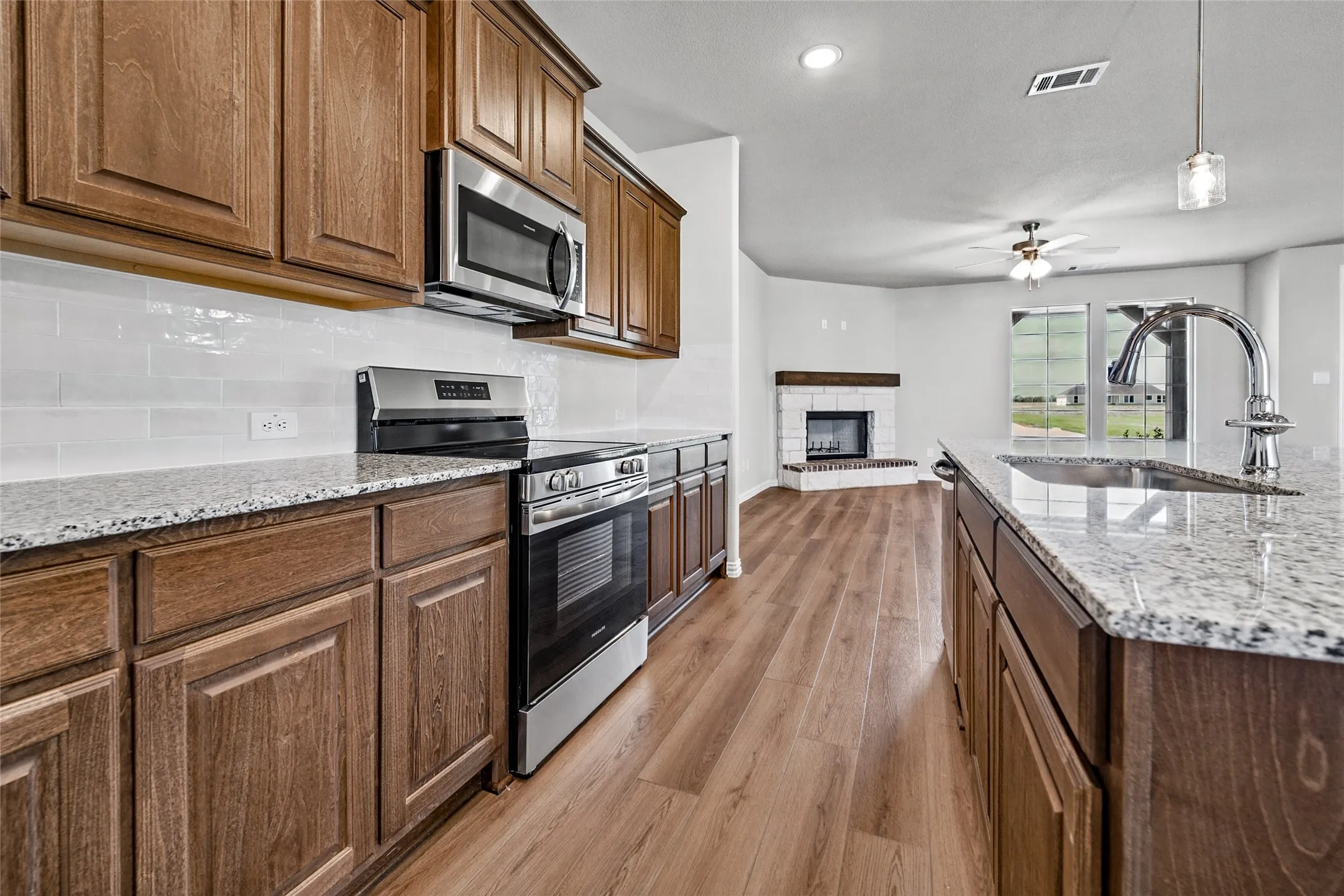 Wood-finish cabinetry with stainless steel appliances, granite-style countertops, white subway tile backsplash, and wood-finish flooring
