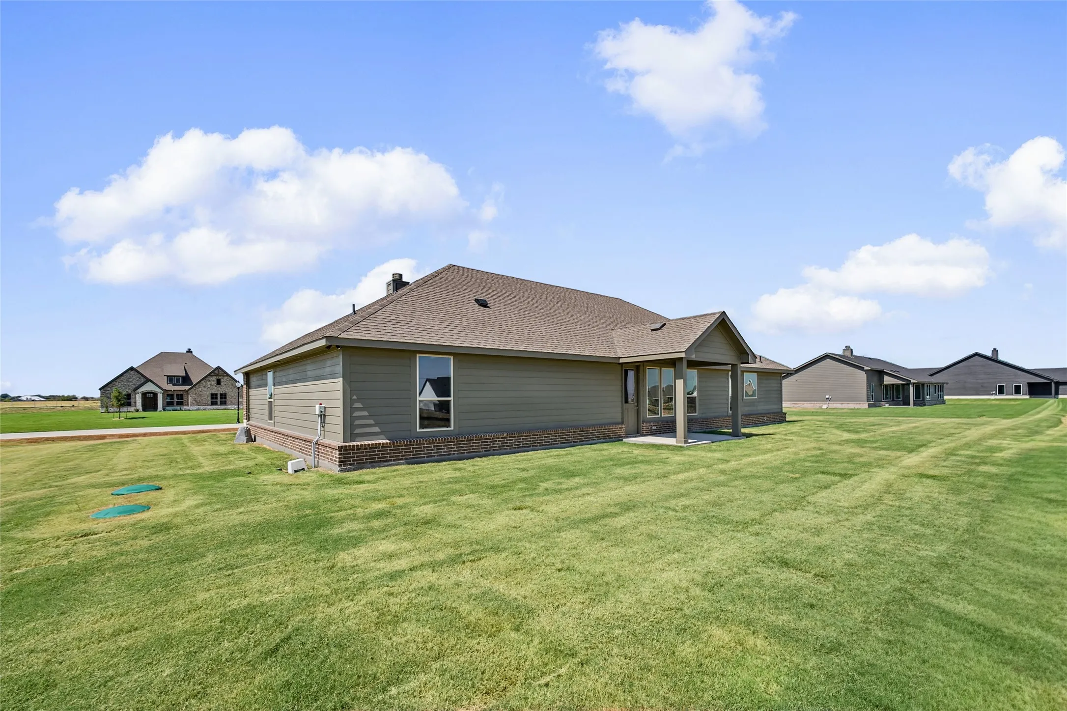 Expansive green lawn surrounds the property, featuring a covered patio with columns and a brick skirting foundation