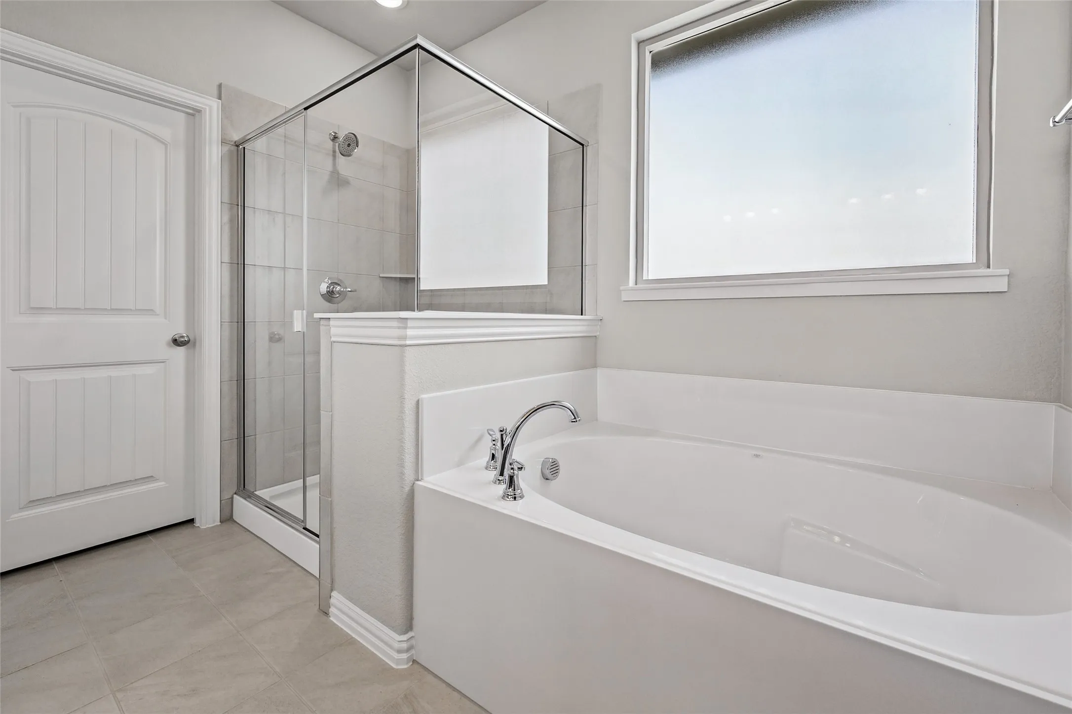 Sleek soaking tub with chrome fixtures, glass-enclosed shower with tiled walls, and large window