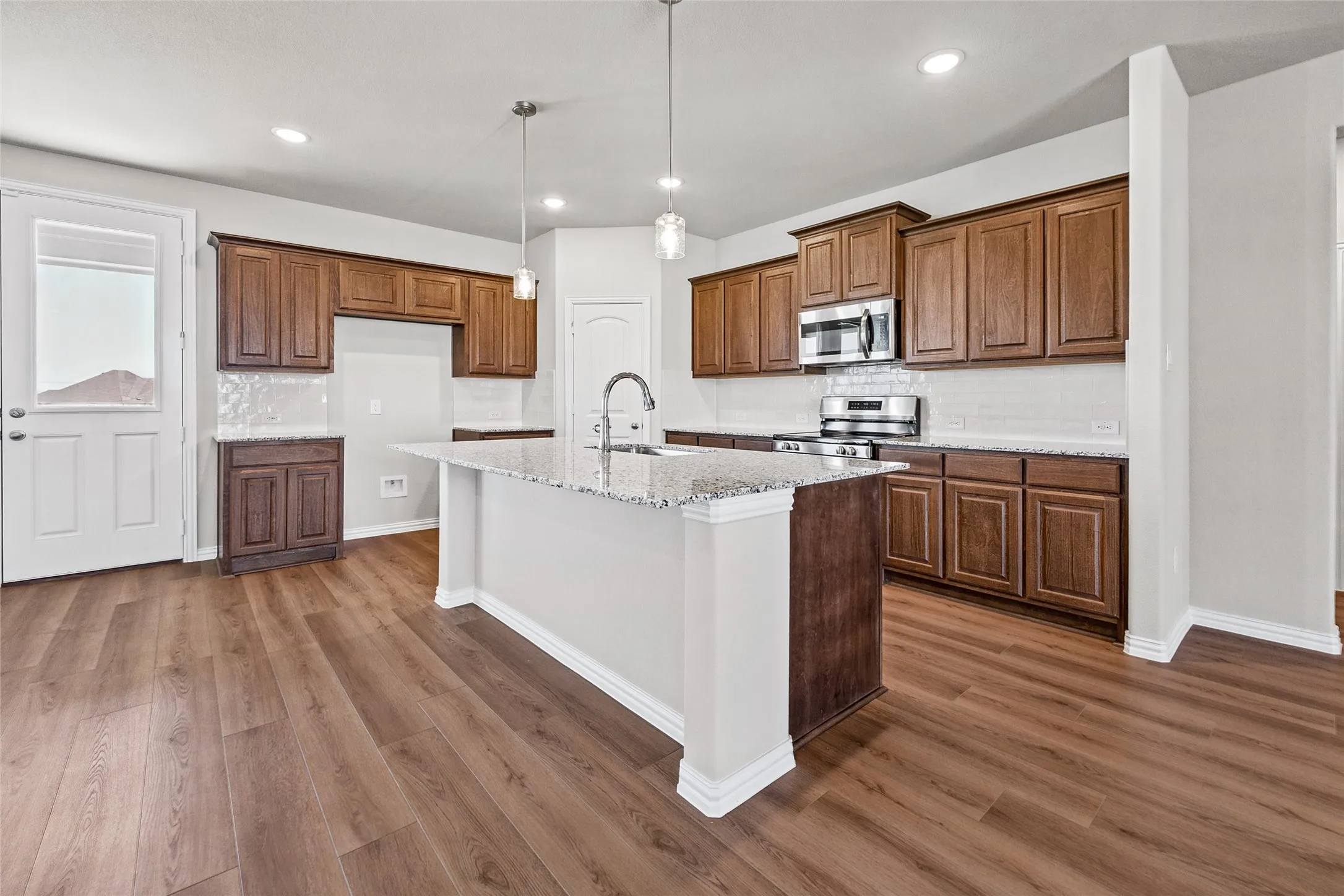 Kitchen featuring wood-finish flooring, recessed lighting, a central island with a granite countertop, wood cabinetry, and stainless steel appliances