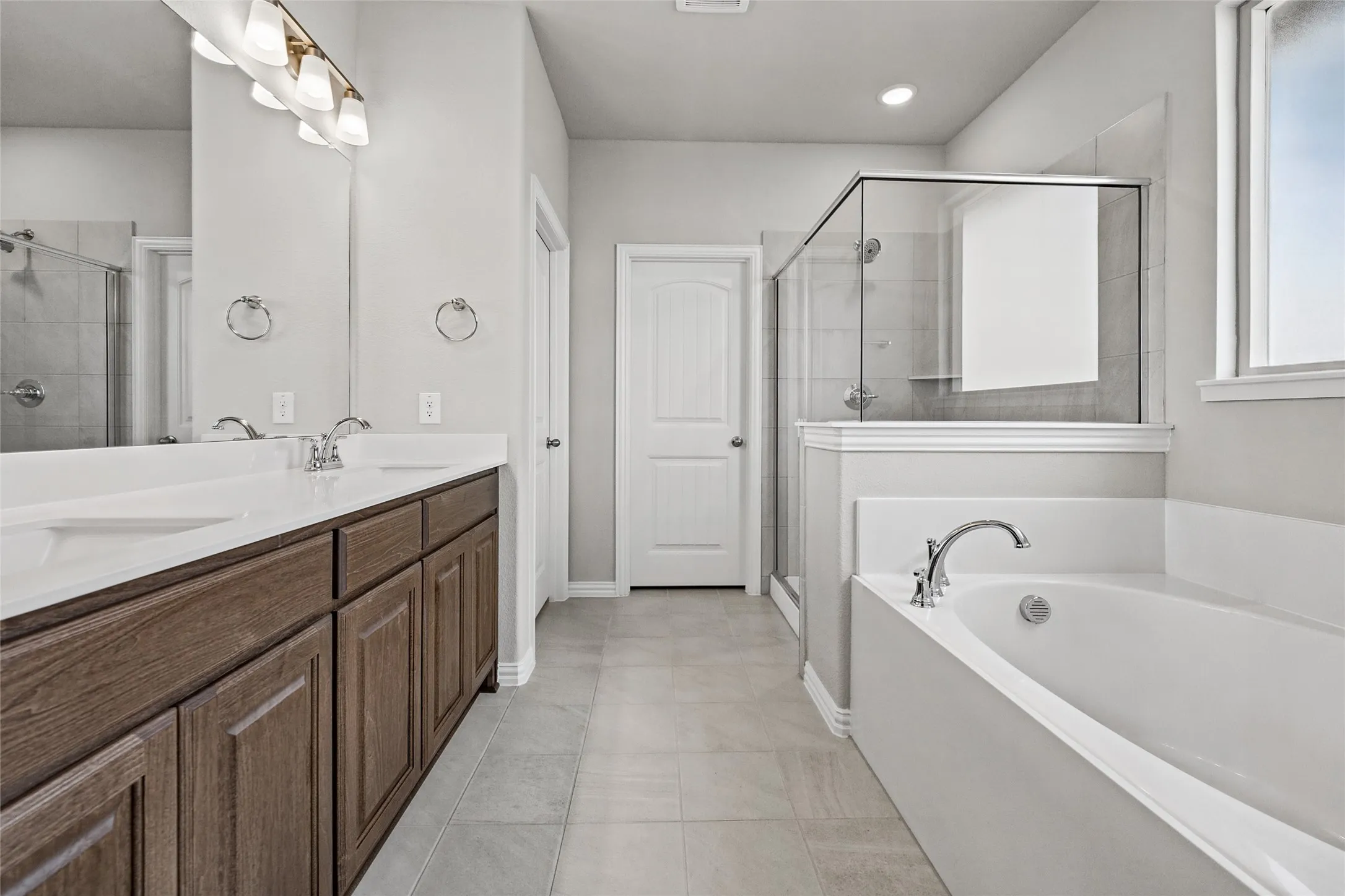 Dual vanity with wood-finish cabinetry, built-in soaking tub, and glass-enclosed shower