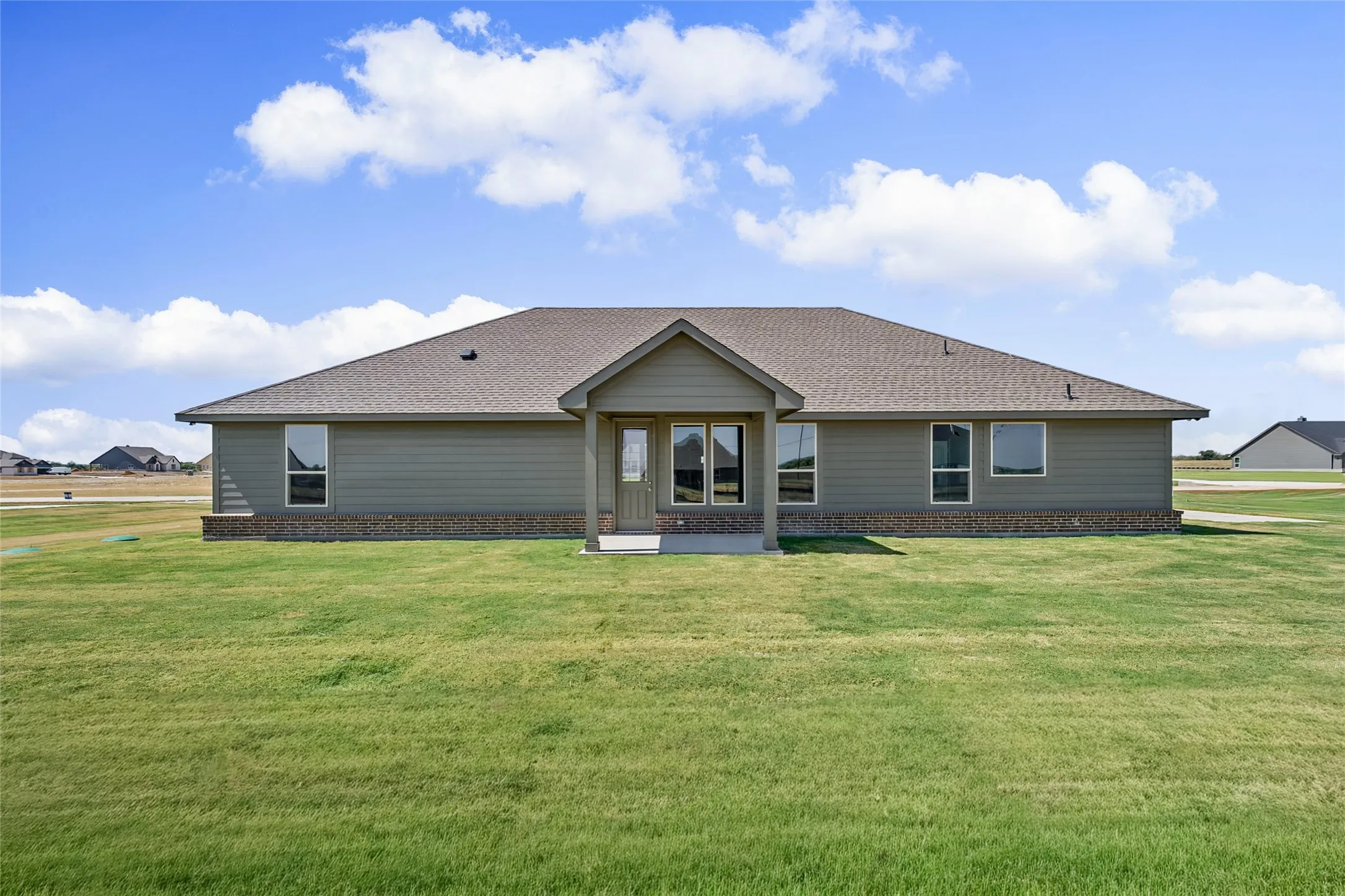 Expansive green lawn, light gray siding, brown brick detailing, multiple windows, and a covered entry