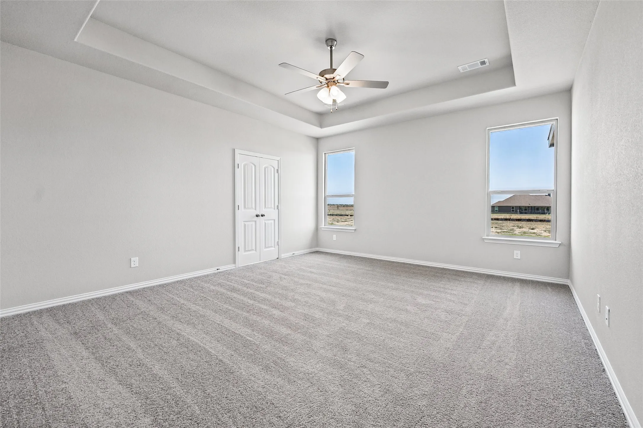 Spacious room featuring tray ceilings, two windows, and light gray carpet