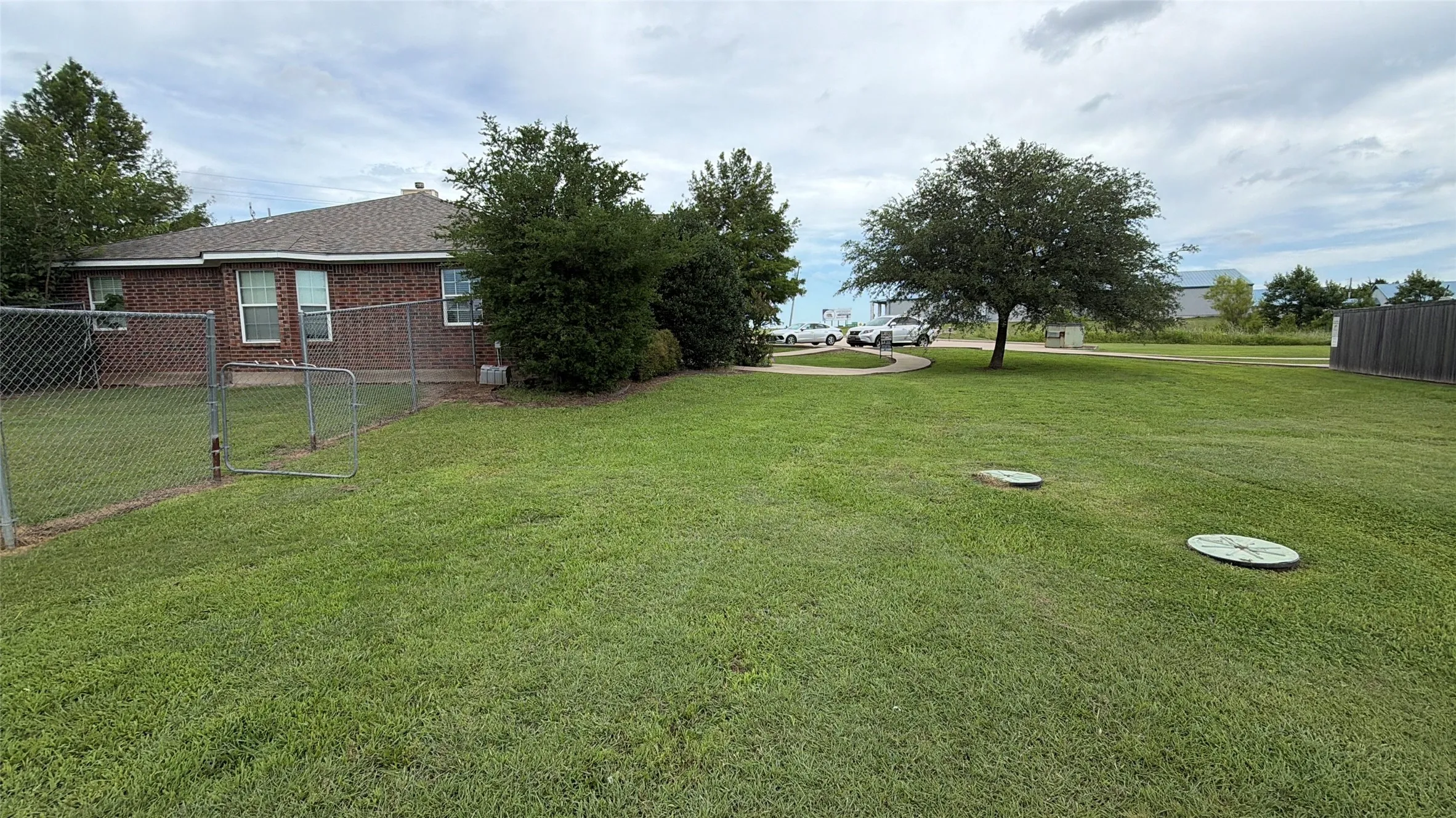 Expansive green lawn with mature trees and a chain-link fence enclosing a portion of the yard