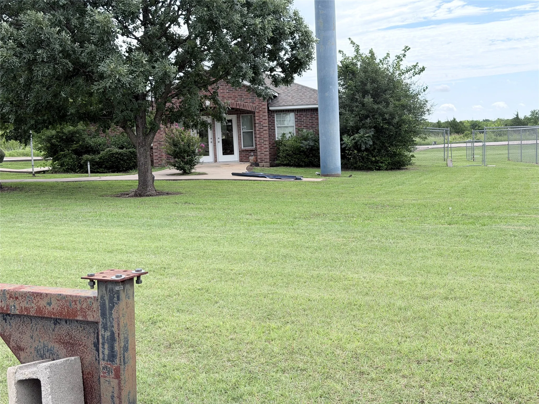 Brick exterior structure with white entry doors, surrounded by established trees and green lawn space