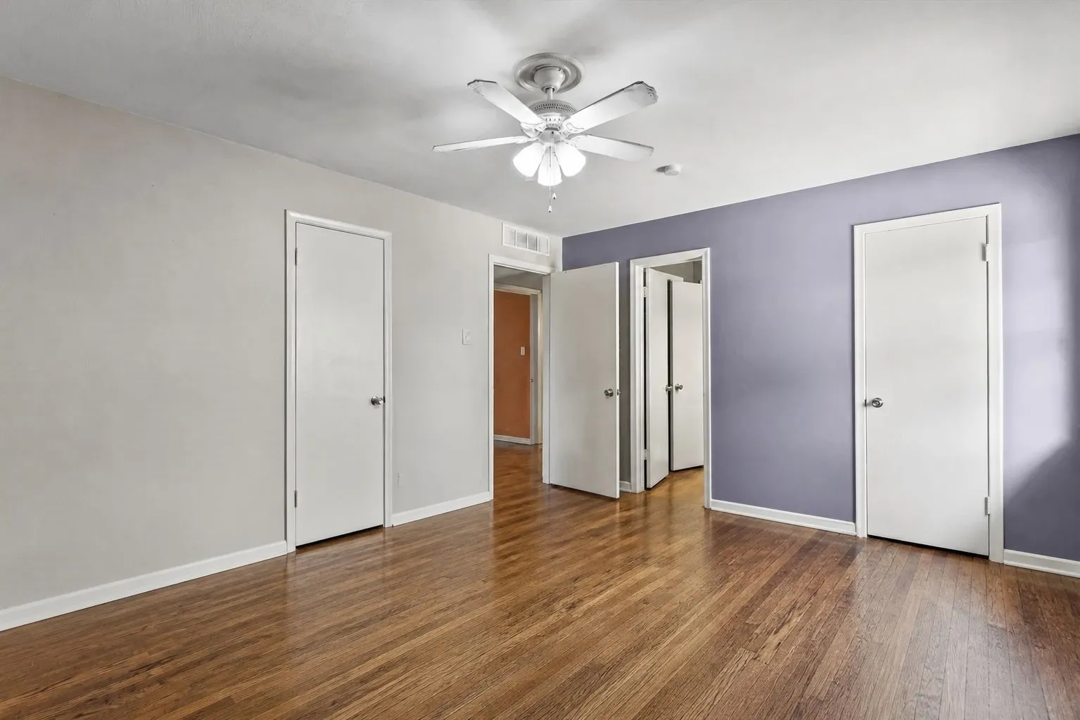 Spacious primary bedroom featuring wood-finish flooring, a ceiling fan, 2 closets and white baseboards. Furniture removed by AI.