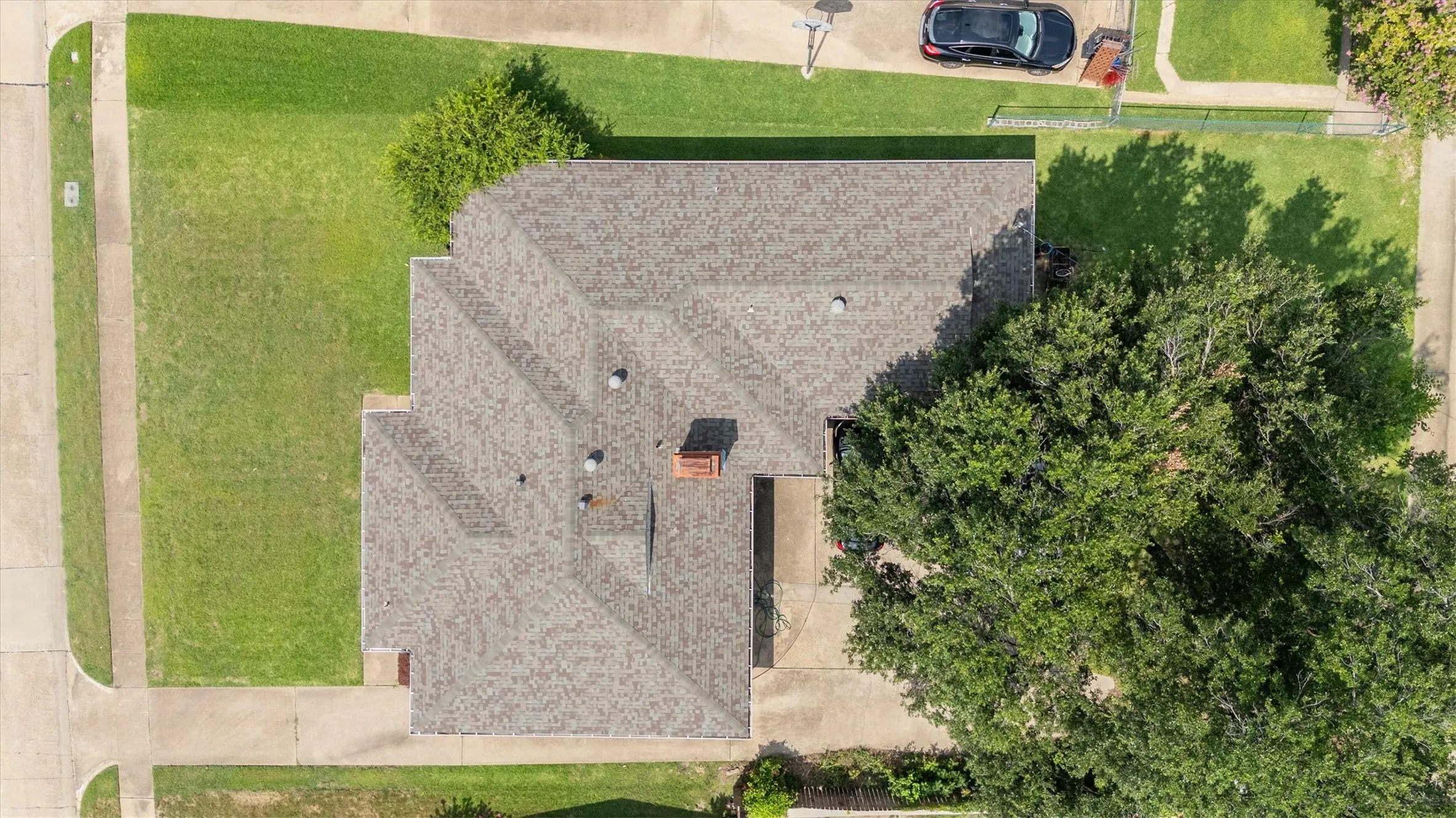 Aerial perspective highlighting the property with a shingled roof, a brick chimney, and multiple roof vents