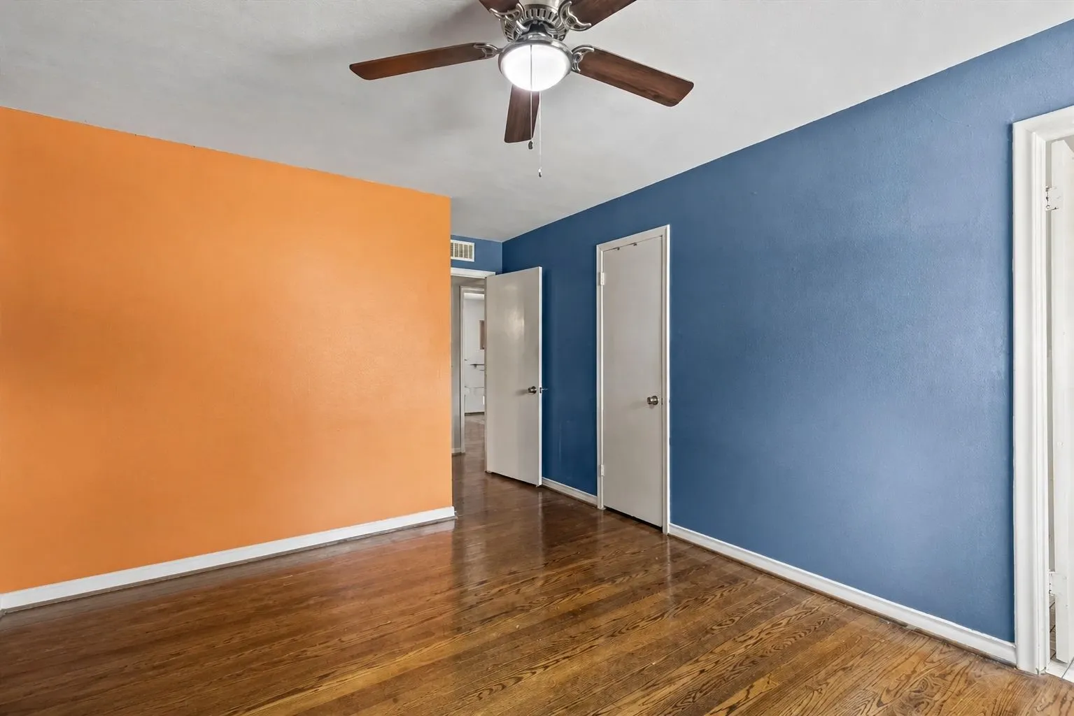 Bedroom featuring wood-finish flooring and a ceiling fan with integrated lighting. Furniture removed by AI.