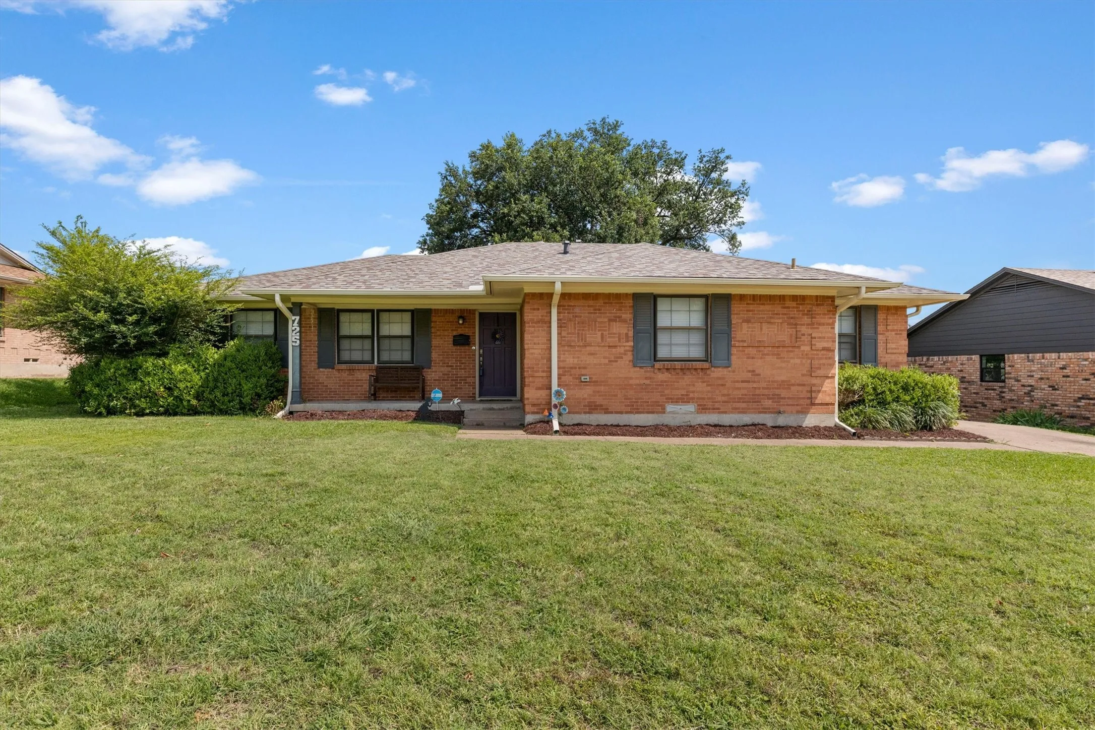 Brick exterior residence with a front porch, grey-toned roof, and a wrap around driveway