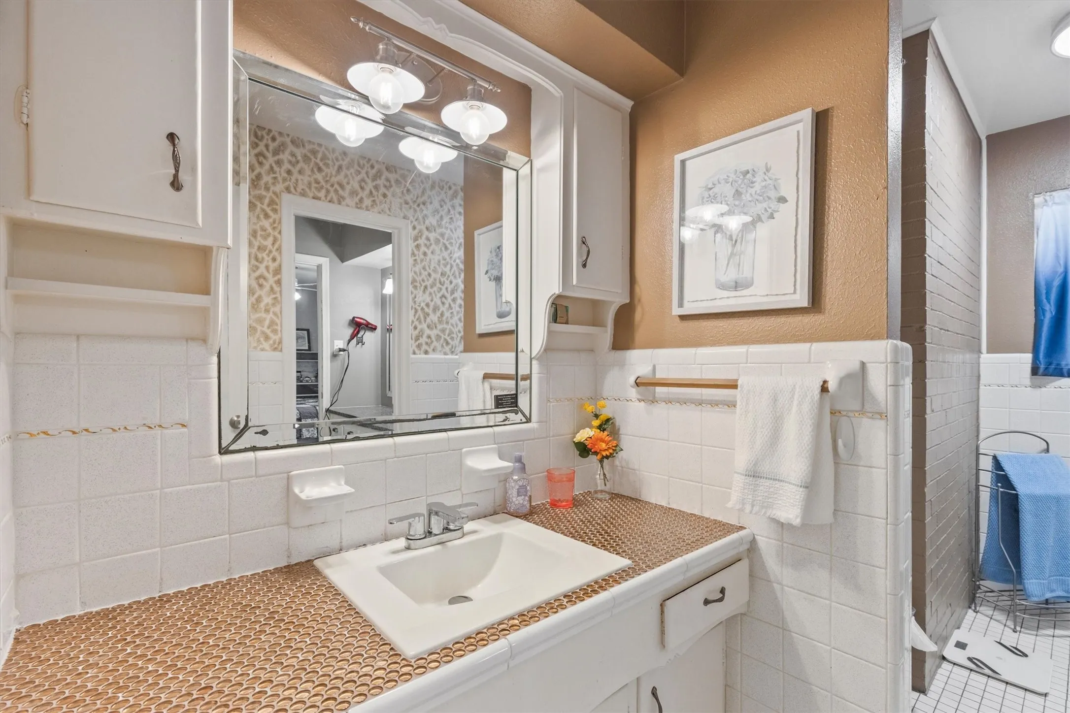 Bathroom vanity featuring a drop-in sink, penny tile countertop, white tile backsplash, framed mirror and medicine cabinets