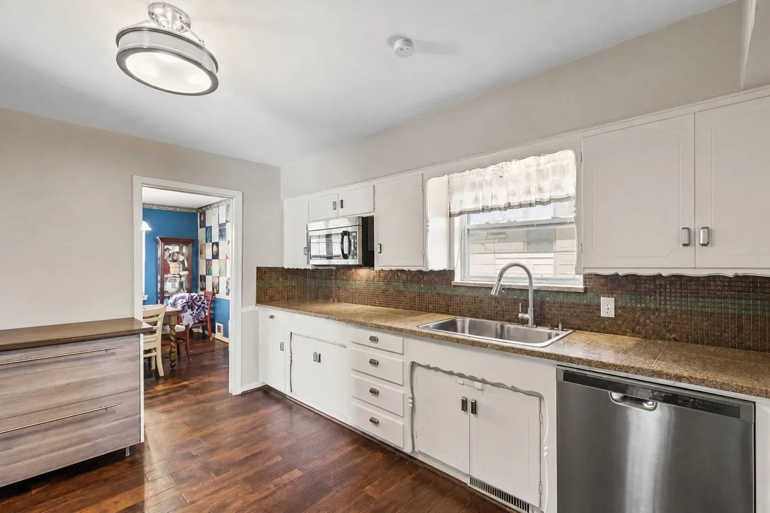 Kitchen featuring rich wood-finish flooring, granite counters, mosaic tile backsplash, white cabinetry, integrated stainless steel dishwasher, and a stainless steel sink with a contemporary faucet. Wall decorations removed by AI.