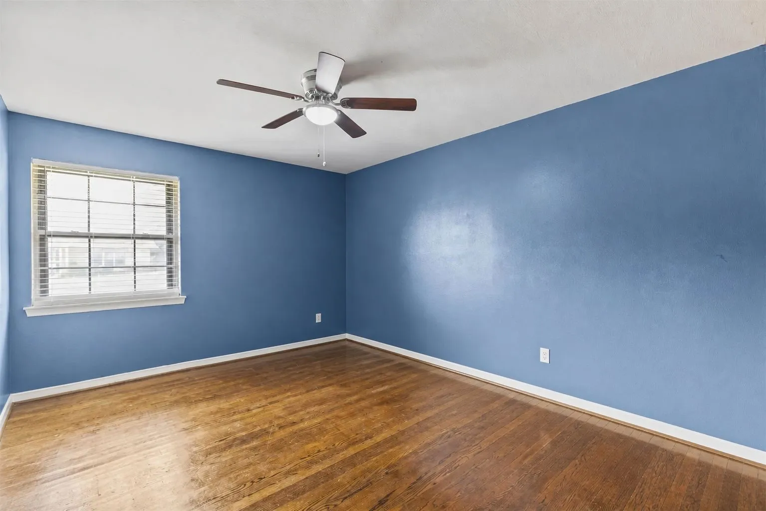 Bedroom featuring wood-finish flooring, a window with horizontal blinds, and a ceiling fan with integrated lighting. Furniture removed by AI.