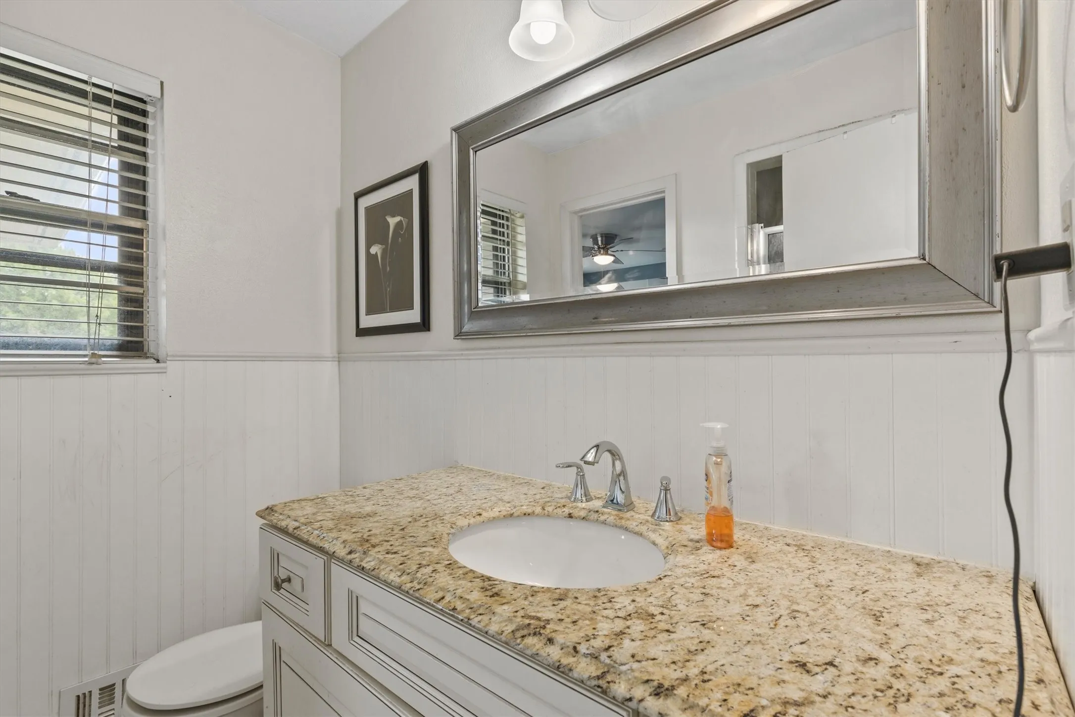 Bathroom vanity featuring a granite countertop, framed mirror, undermount sink, and chrome faucet