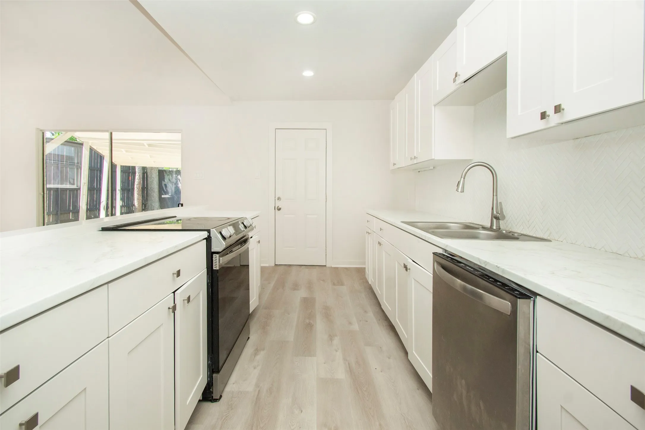 Kitchen featuring white cabinetry, appliances with stainless steel finishes, light hardwood / wood-style flooring, light stone counters, and sink