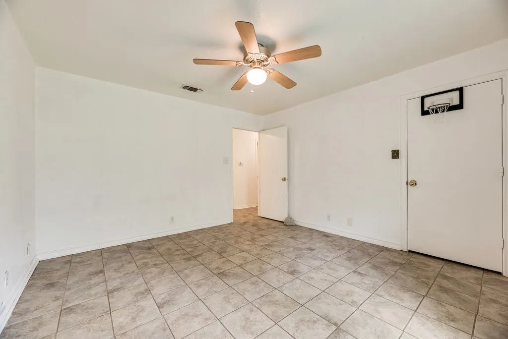Spacious interior room featuring tile flooring, white walls, and a ceiling fan with light fixture